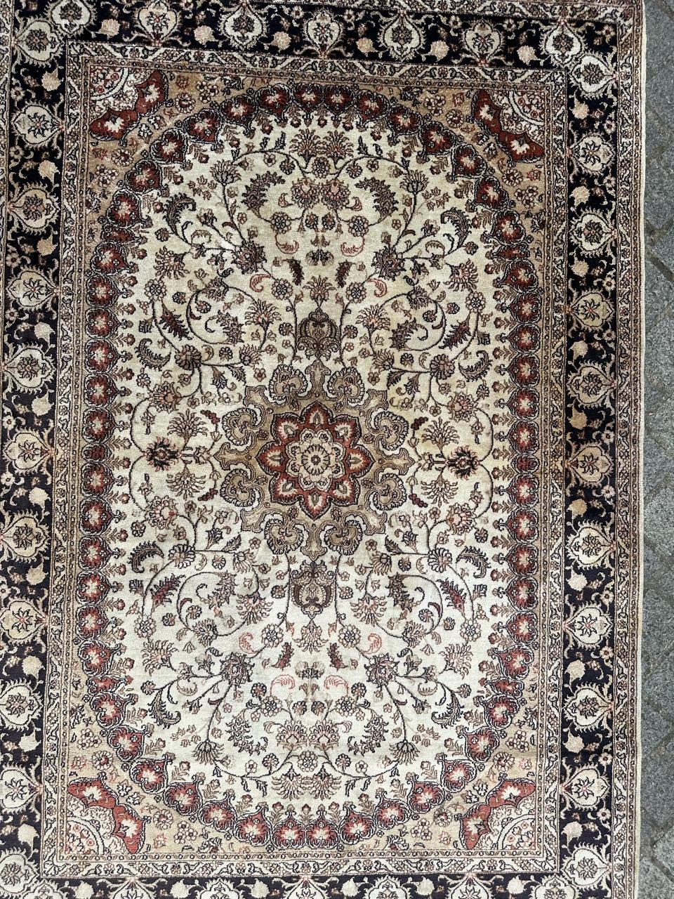Exquisite vintage Persian Tabriz-style rug, meticulously hand-knotted with silk on silk, boasting a delicate floral design. In the center, a red and light green floral medallion is surrounded by deep black lines. The white field is adorned with
