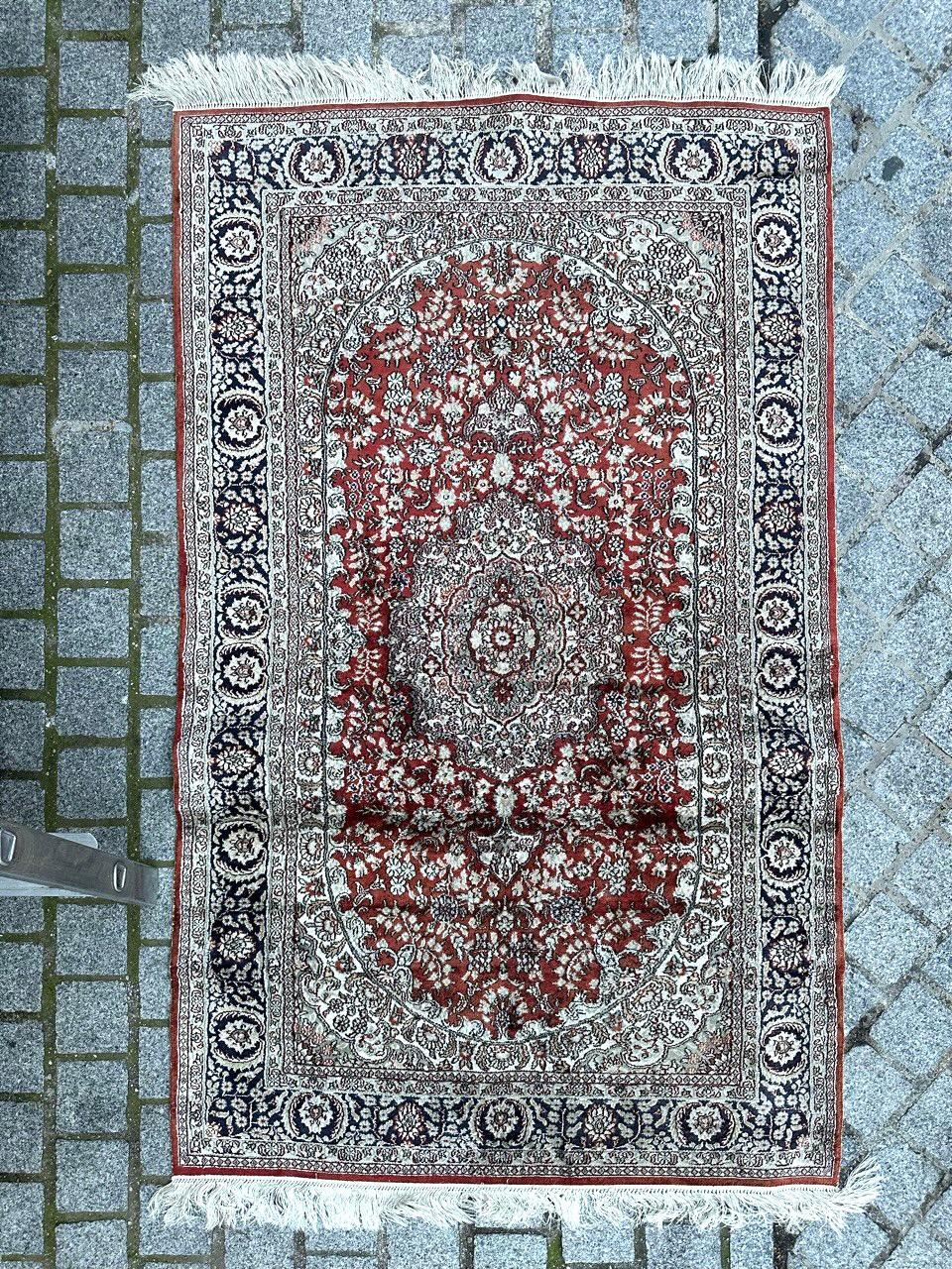 Exquisite vintage Persian Tabriz-style rug, meticulously hand-knotted with silk on silk, boasting a delicate floral design. In the center, a white and light green floral medallion is surrounded by deep blue lines. The vibrant reddish-orange field is
