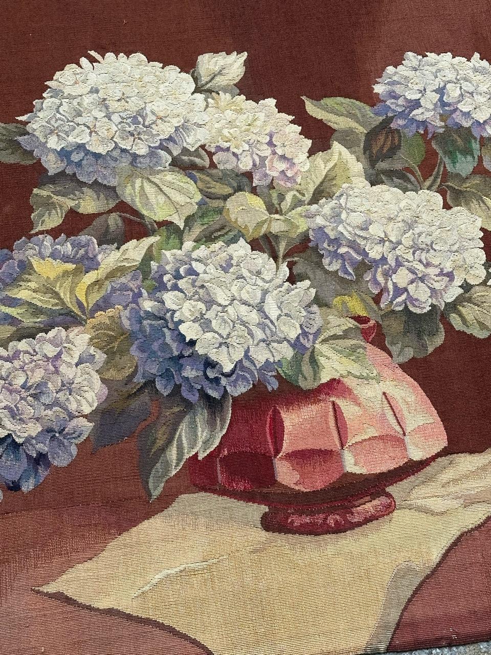 Entdecken Sie die zeitlose Eleganz dieses exquisiten französischen Aubusson-Teppichs aus der Mitte des Jahrhunderts. Das bezaubernde Design mit einem Blumentopf auf einem Tischtuch zeigt eine schöne Pflanze mit violetten Blüten und grünen Blättern