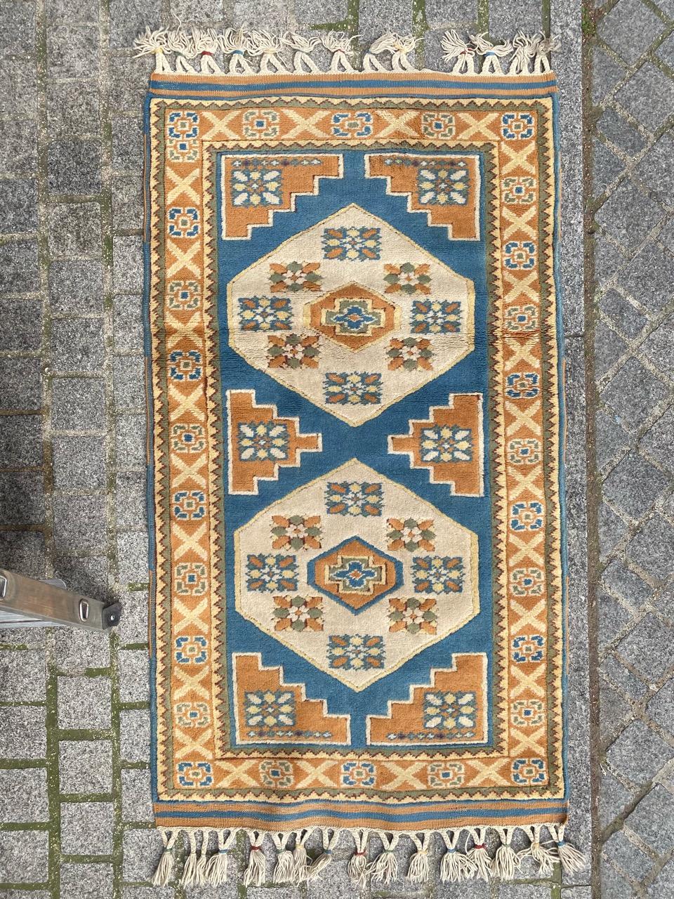 Exquisite Turkish rug from the late 20th century, meticulously handwoven with wool on wool, featuring intricate geometric designs. The central field boasts two geometric white medallions on a sky-blue background with vibrant orange motifs. It is