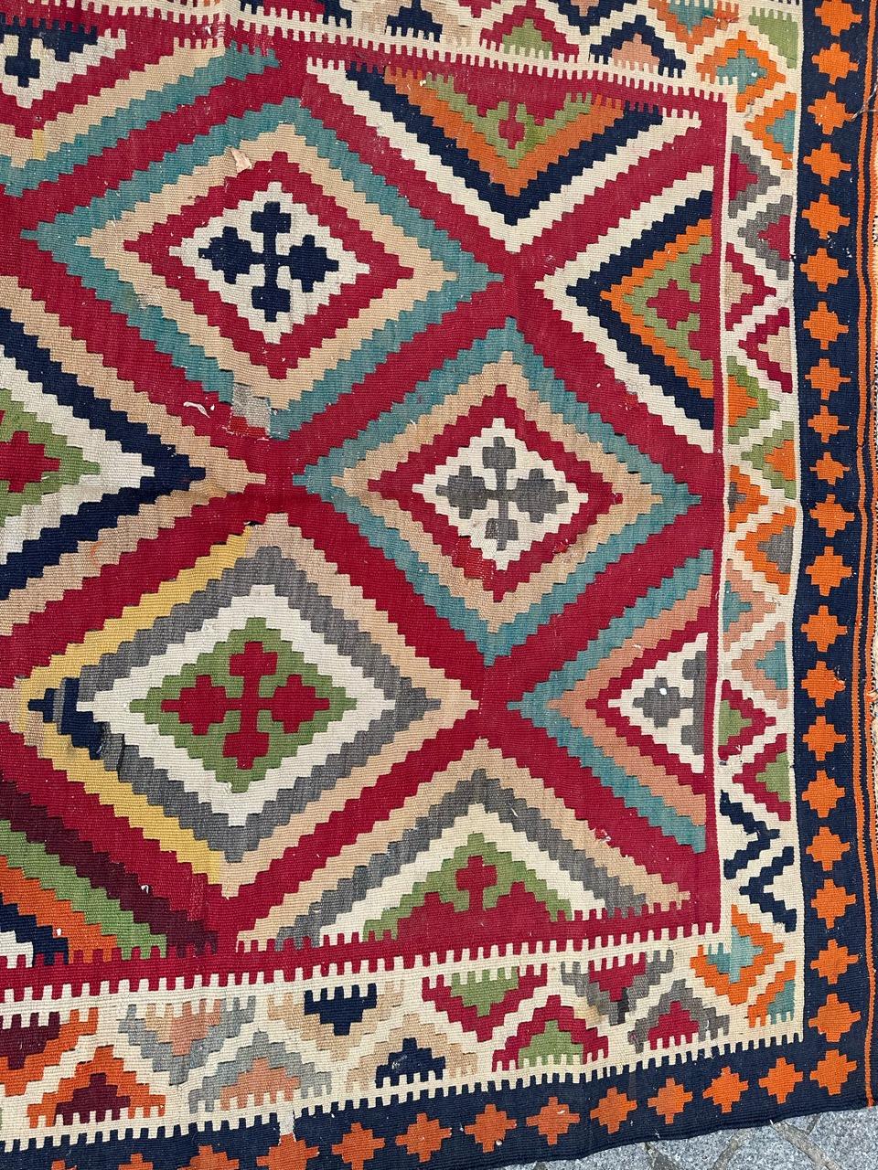 Exquisite Qashqai antique Kilim, meticulously handwoven with wool on a cotton foundation. Featuring a captivating geometric and tribal design, the vibrant red backdrop showcases interconnected diamonds adorned with stylish patterns in green, orange,