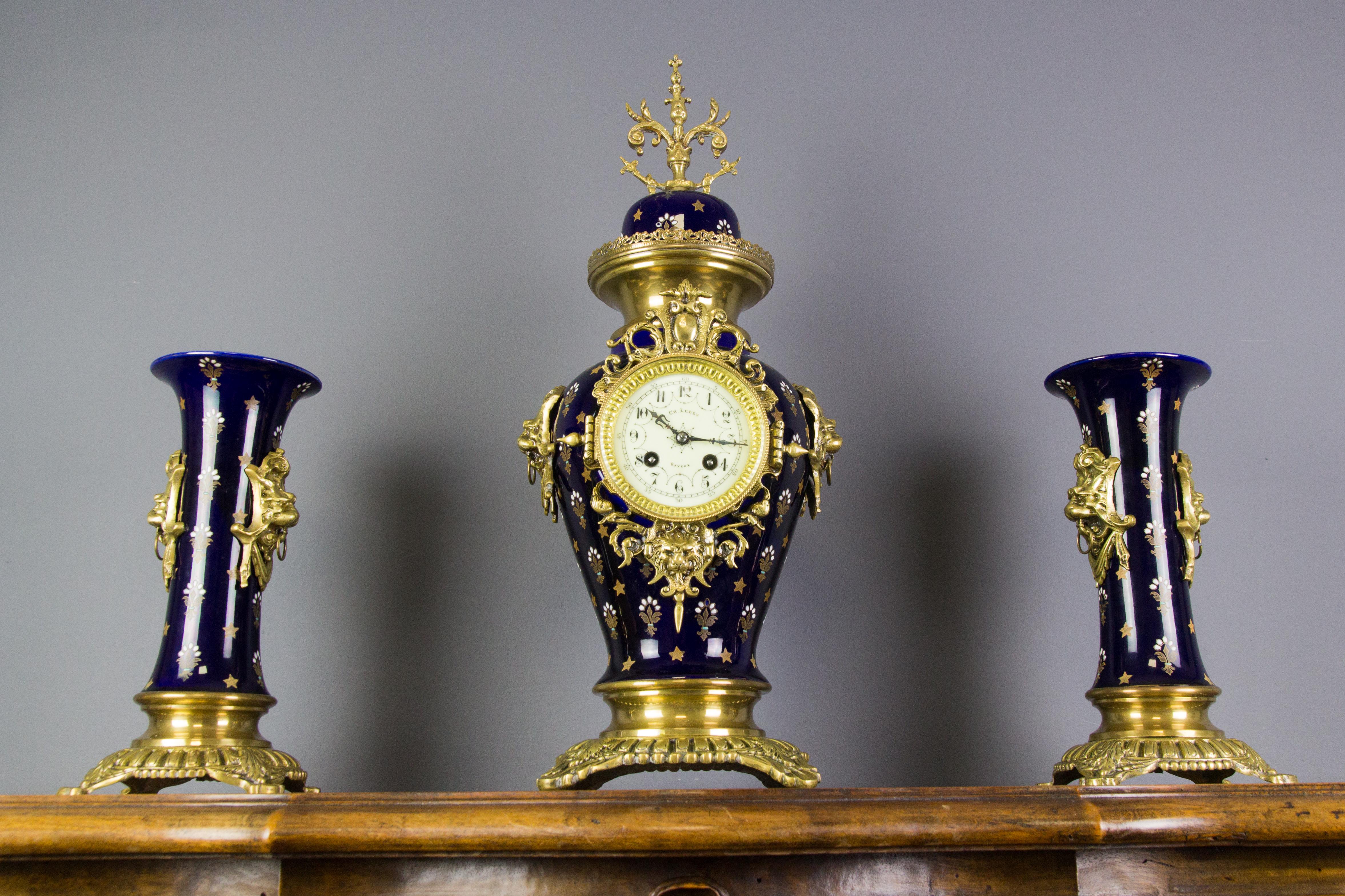 An impressive antique Belgian Boch Frères Keramis pottery 3-piece clock set includes a clock and two vases on ornate bronze bases and is decorated with lion heads on the sides. This pottery and bronze, the brass-mounted set was done in a deep royal