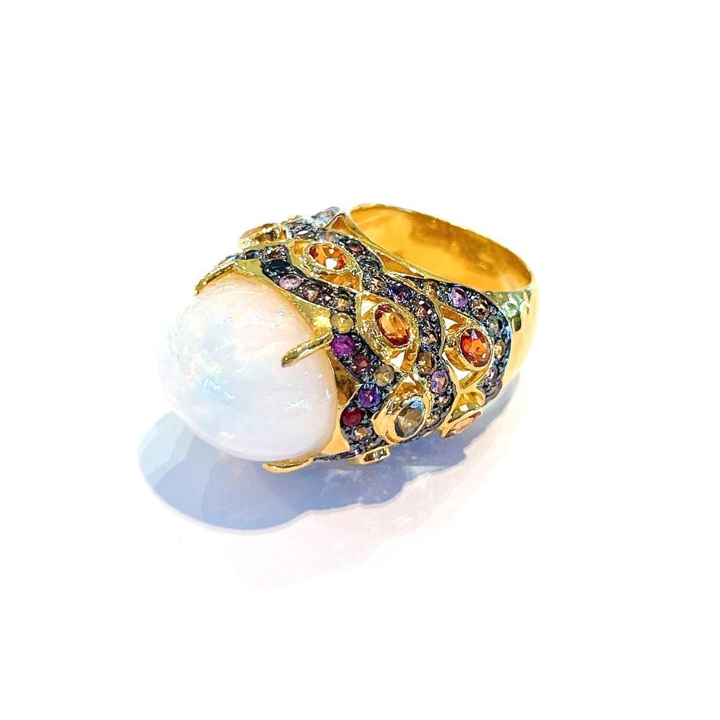 Bochic “Capri” Natural White Opal & Sapphires Ring Set in 18K Gold & Silver 
Natural White Opal Cabochon - 12 Carats 
Natural Multi color sapphires from Sri Lanka, round brilliant shapes - 5 carats 

This Ring is from the 