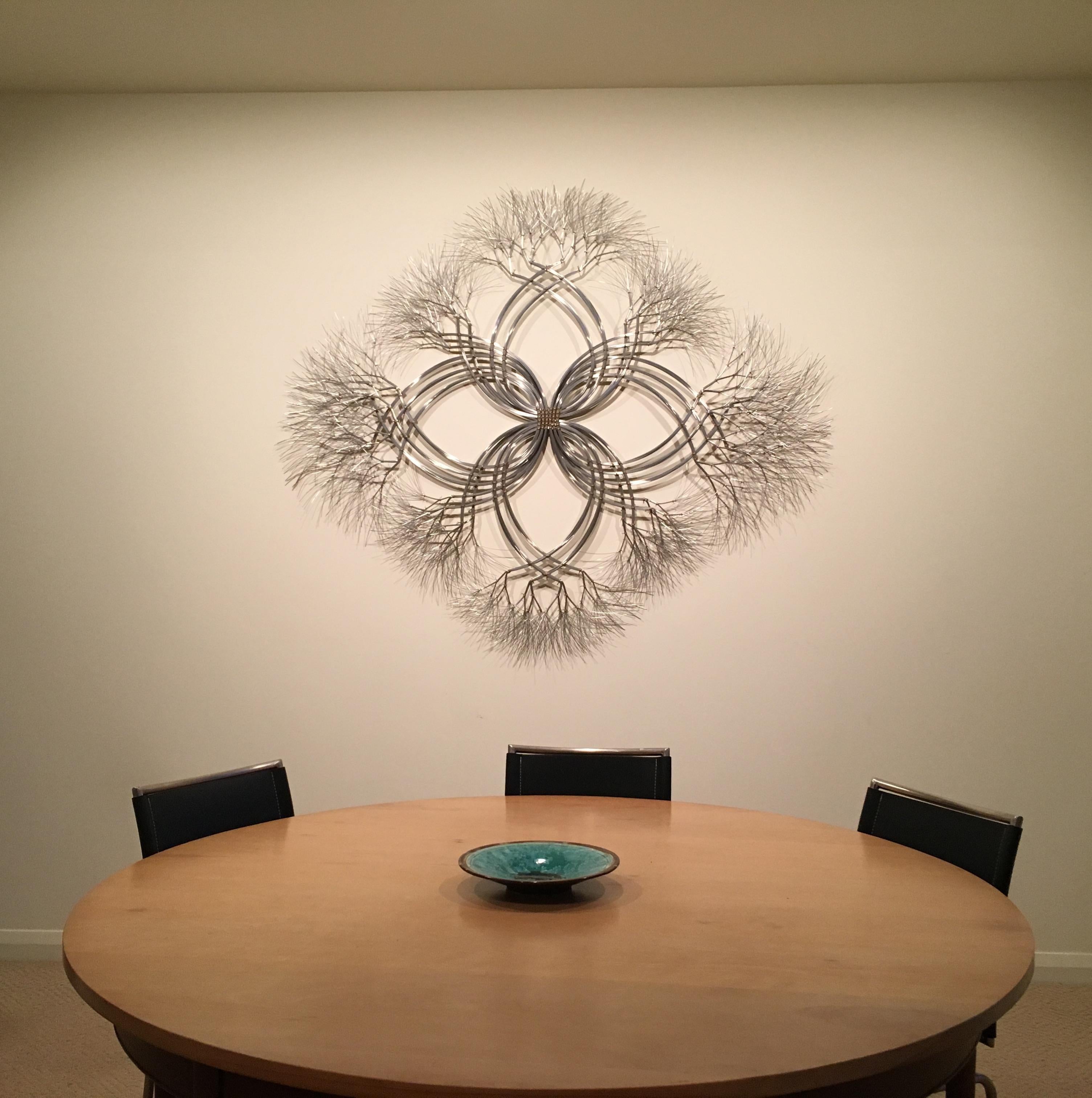 This wall mounted sculpture is created using bronze and stainless steel wire. Kue uses an aesthetic reminiscent of trees, electricity, and light to create sculptures of peace and beauty. Adults and children alike see snowflakes, trees, flowers,