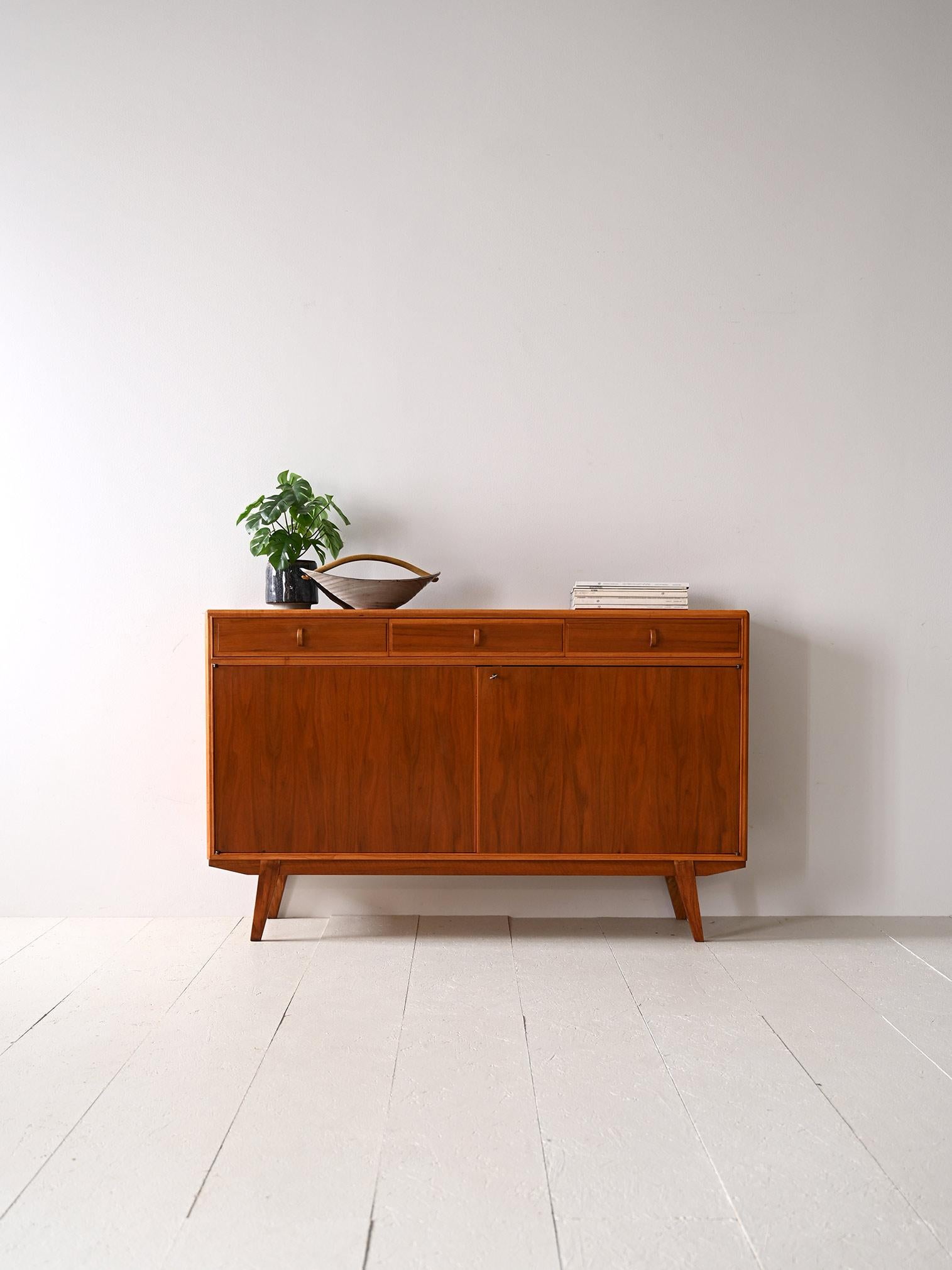 Scandinavian teak sideboard from the 1960s.

A Swedish design piece with a compact and modern shape, consisting of a storage compartment closed by hinged doors above which are three drawers with a curved wooden handle.
Inside the cabinet are two