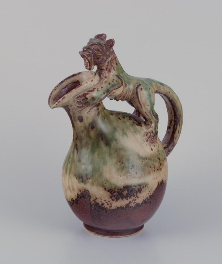 Bode Willumsen for Royal Copenhagen. 
Ceramic pitcher in sung glaze. Handle in the shape of a mythical creature.
Model number: 20128
1930s/1940s.
Marked.
Perfect condition.
First factory quality.
Dimensions: W 18.0 cm x H 23.0 cm.
