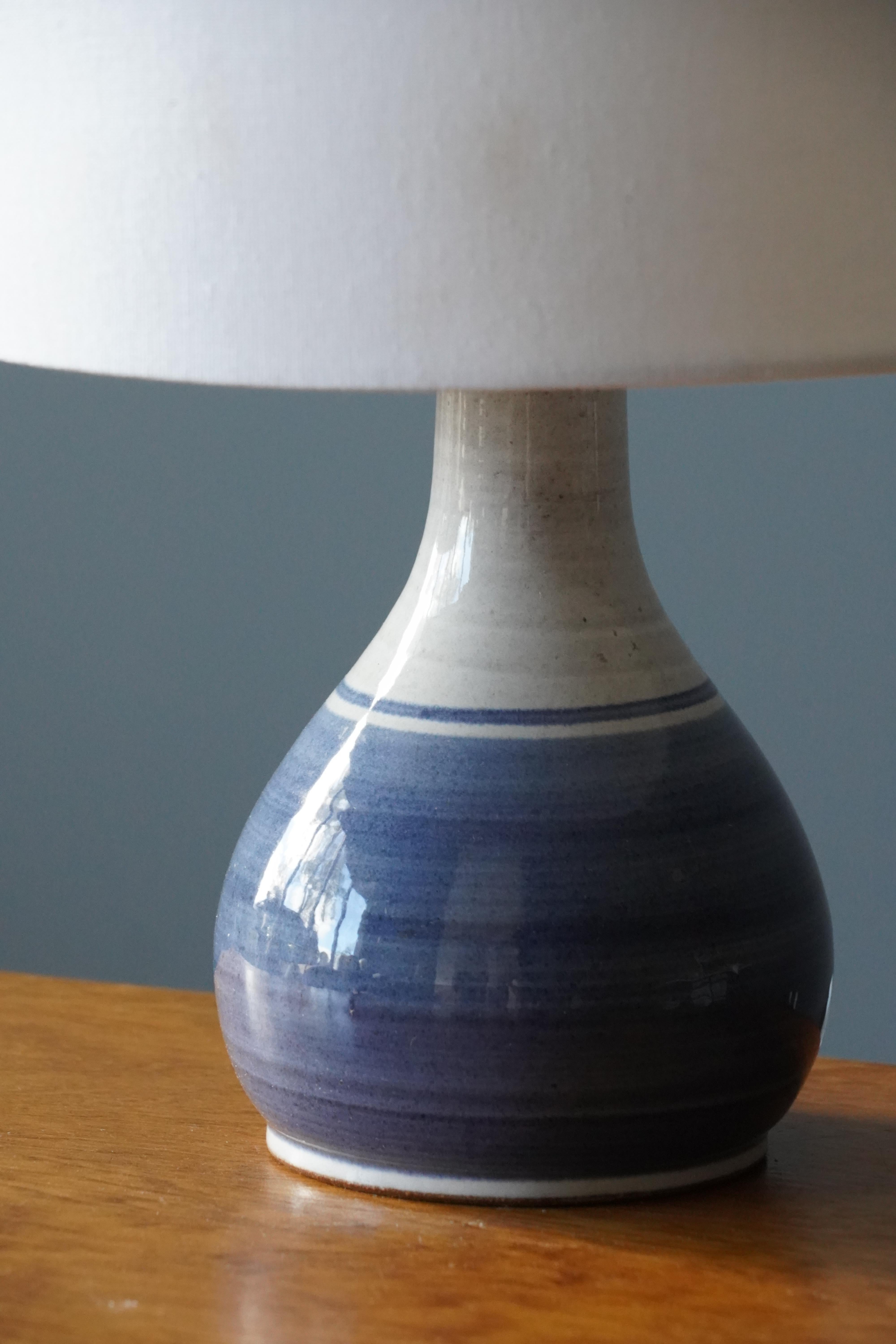 A table lamp, designed and produced by Bofa, Denmark, c. 1960s. Features blue and white glazed stoneware.

Dimensions listed are without shade. 
Dimensions with shade: height is 14 inches, width is 10 inches.
Dimensions of shade: top diameter is