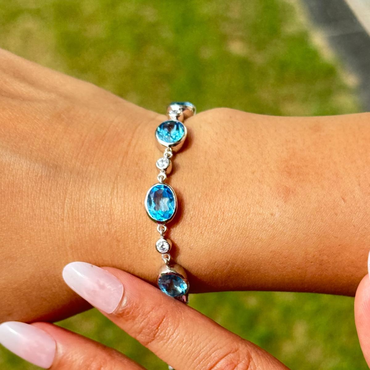 Questo braccialetto Bohe Oval Blue Topaz regolabile con chiusura scorrevole e pietre CZ bianche è uno squisito braccialetto bolo in argento sterling 925, incastonato ad arte con cinque vivaci gemme di topazio blu dal taglio ovale. Ogni pietra blu