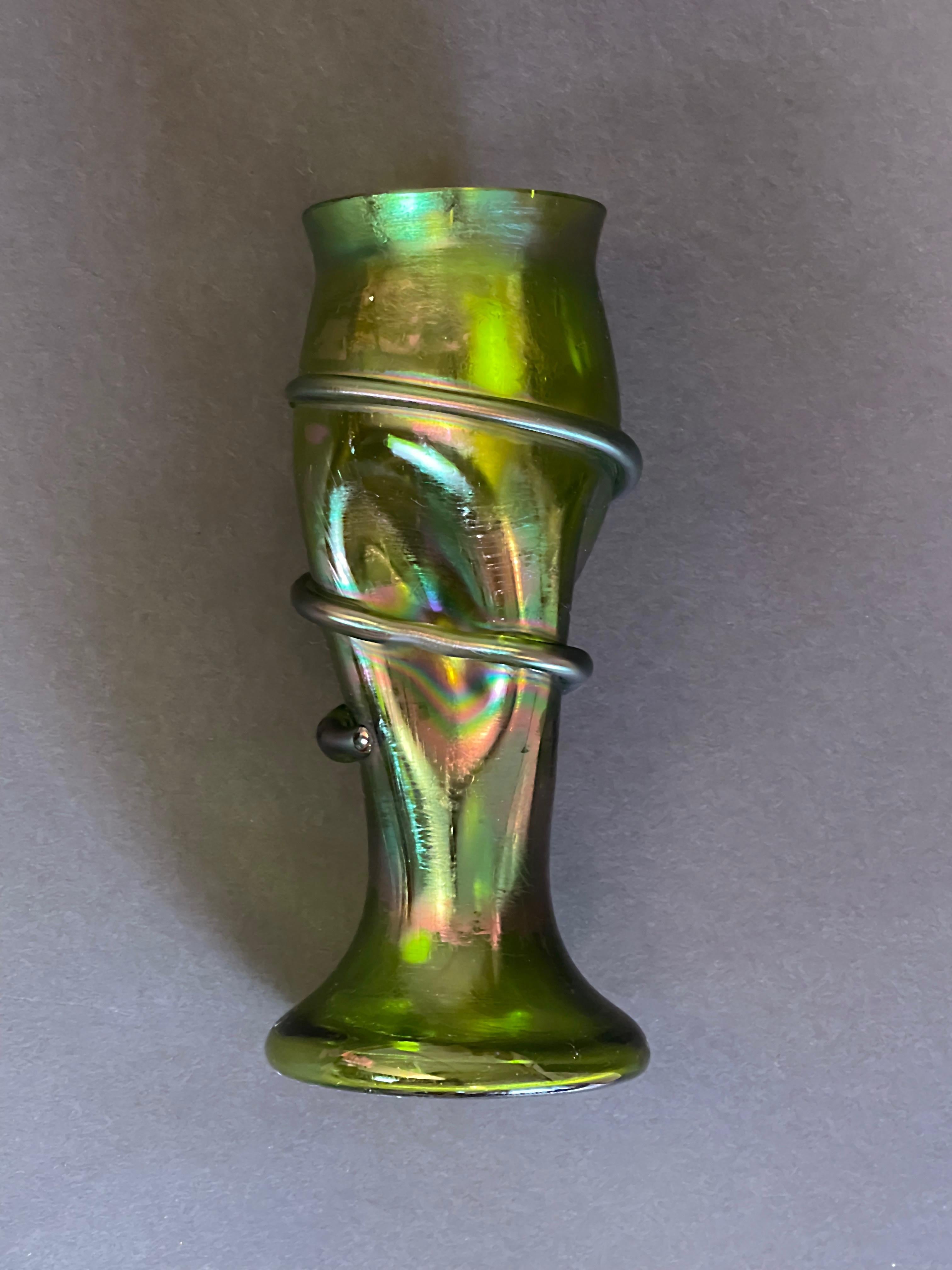 Fantastic design vase attributed to Josef Rindskopf, Bohemia, around 1900.
Here in an olive green with an iridescent finish – shimmering sometimes more, sometimes less, depending
on the light that shines onto it.
A snake winding its way downwards,