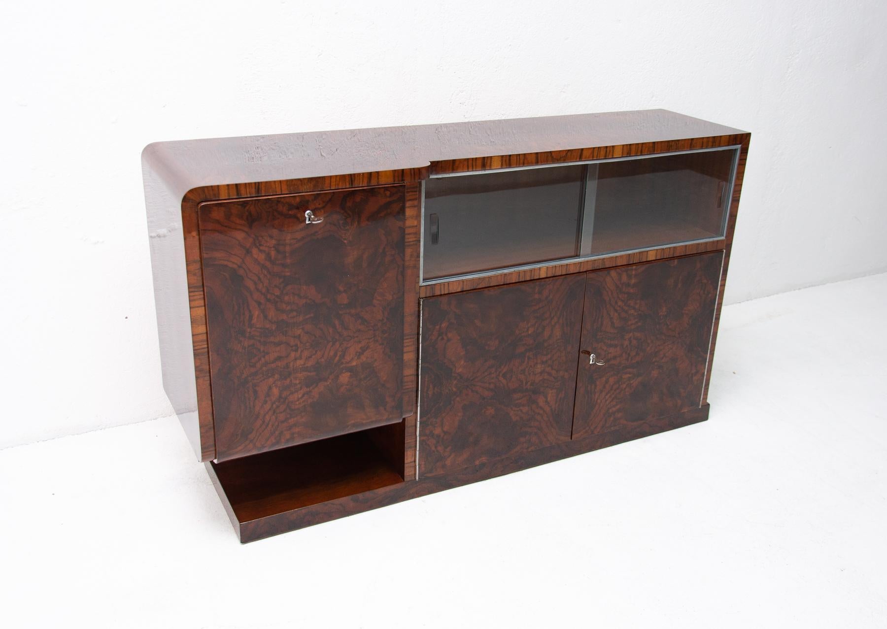 Bohemian functionalist glazed sideboard in walnut veneer. It was made in the 1930s. It features a very simple and practical design. Standing on a massive rectangular base. Consists of two drawers and two side storage space. One of them can be used