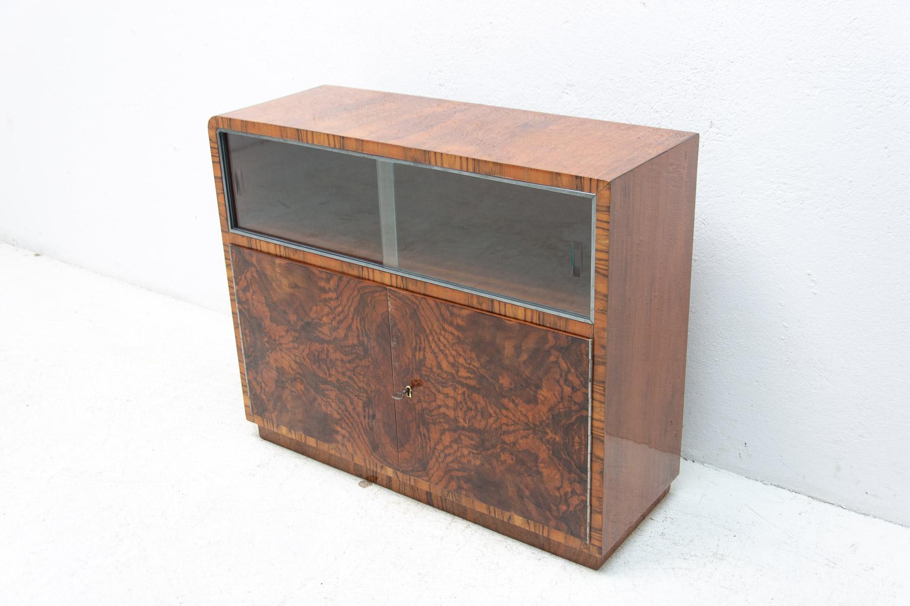 Bohemian glazed bar or sideboard in walnut veneer from the Art Deco period. It wase made in the 1930´s. It features a very simple and practical design. Standing on a massive rectangular base. Consists of two storage spaces, one is glazed and the