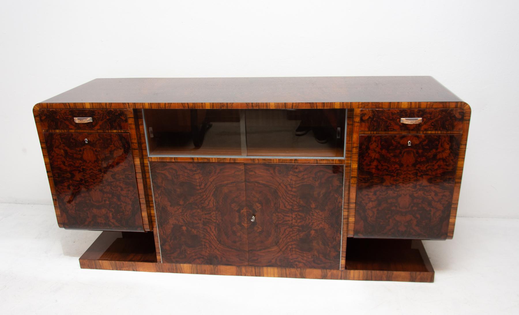 Bohemian buffet or sideboard in walnut veneer from the Art Deco period. It was made in the 1930s. It features a very simple and practical design. Standing on a massive rectangular base. Consists of two drawers with chromed handles and two side