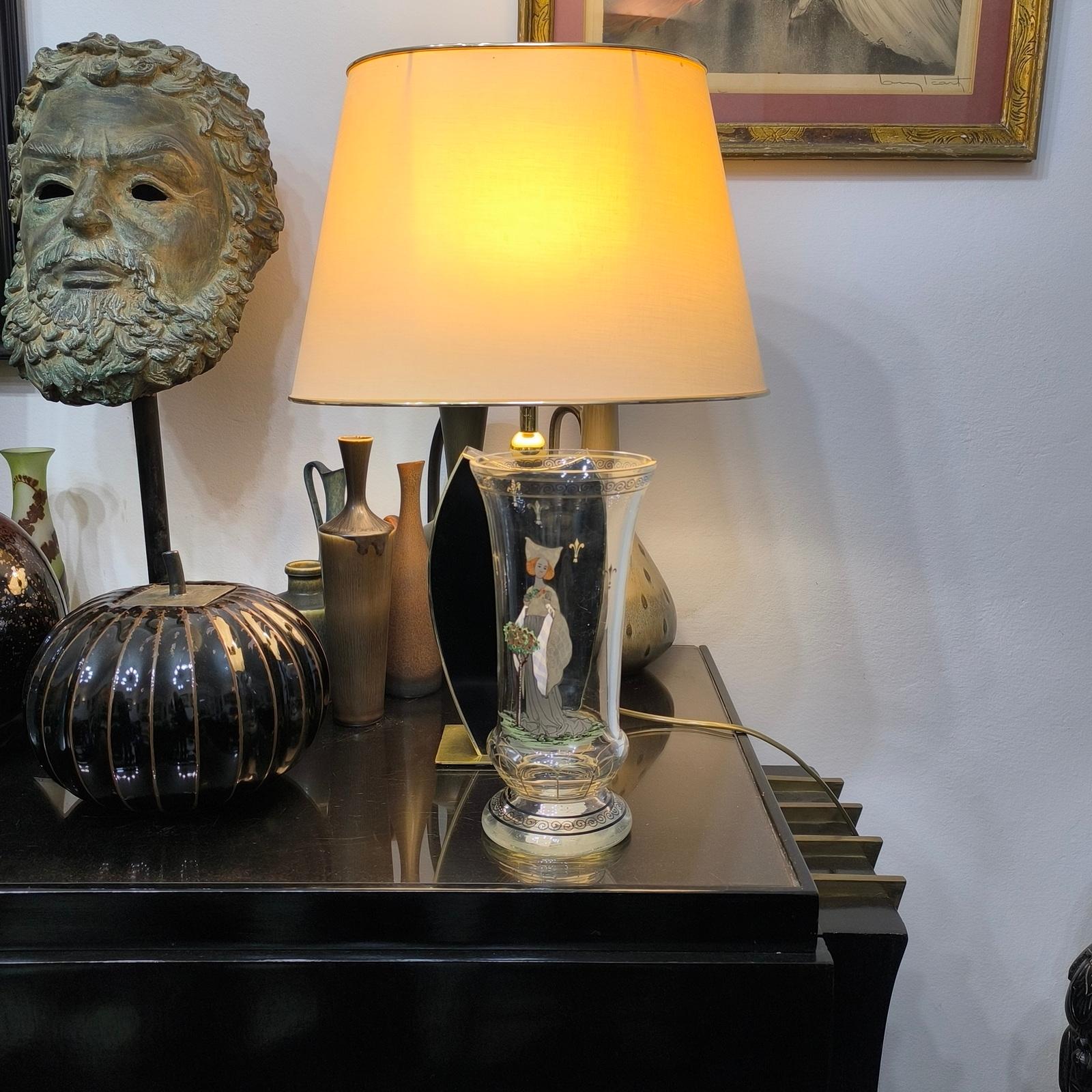 Stunning Bohemian pedestal glass vase with 'schwarzlot' (black ink) and gold designs with front decoration of a young woman in medieval costume, next to a blooming tree.
Haida Steinschönau Fachschule and dating from the early 20th century. 
Height
