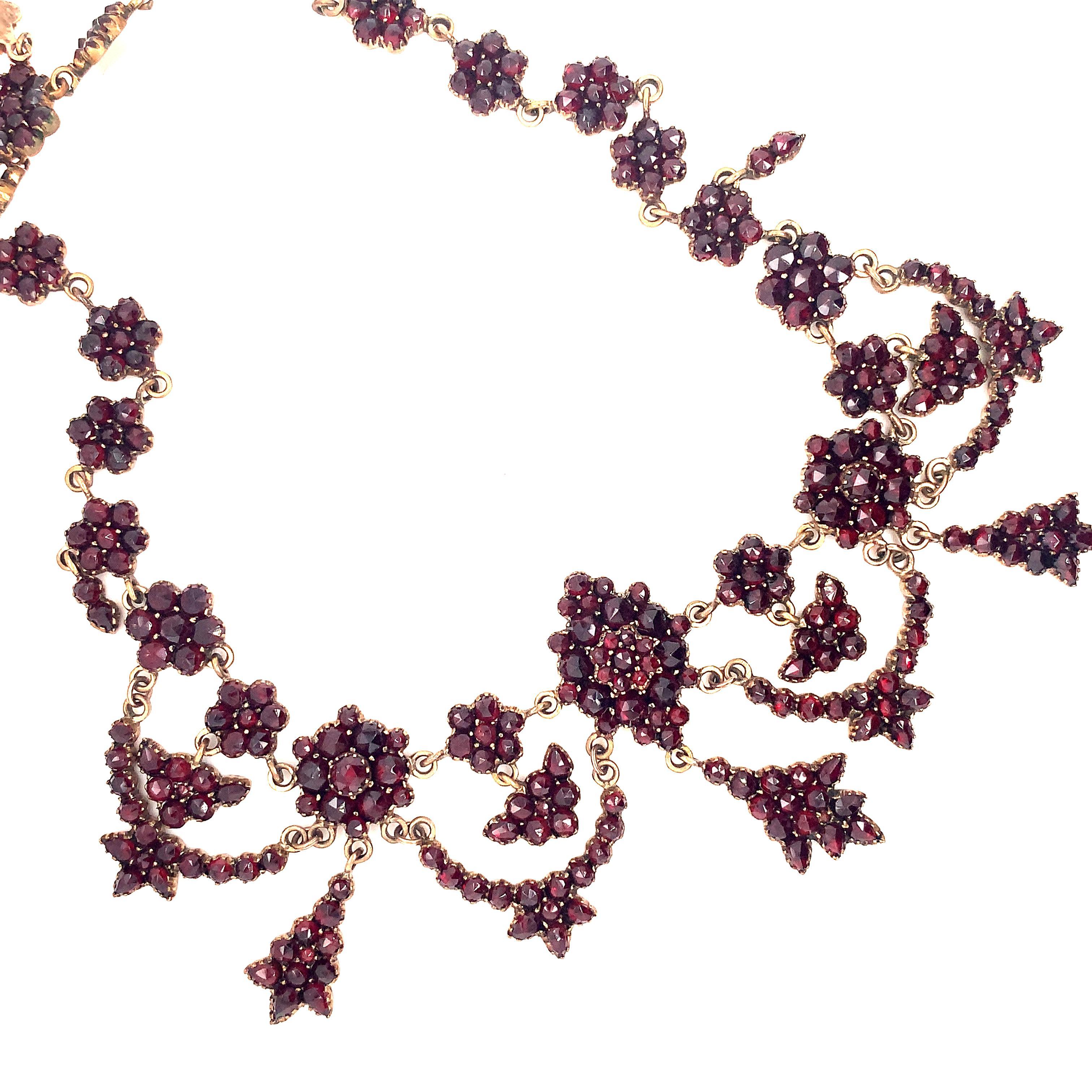 Victorian gilt jewelers brass Bohemian garnet necklace with rose cut garnets.There is a larger oval rosette in the center with a drop, 2 medium rosettes with drops and 4 swags. There are 26 small rosettes and a rectangular garnet clasp. The necklace