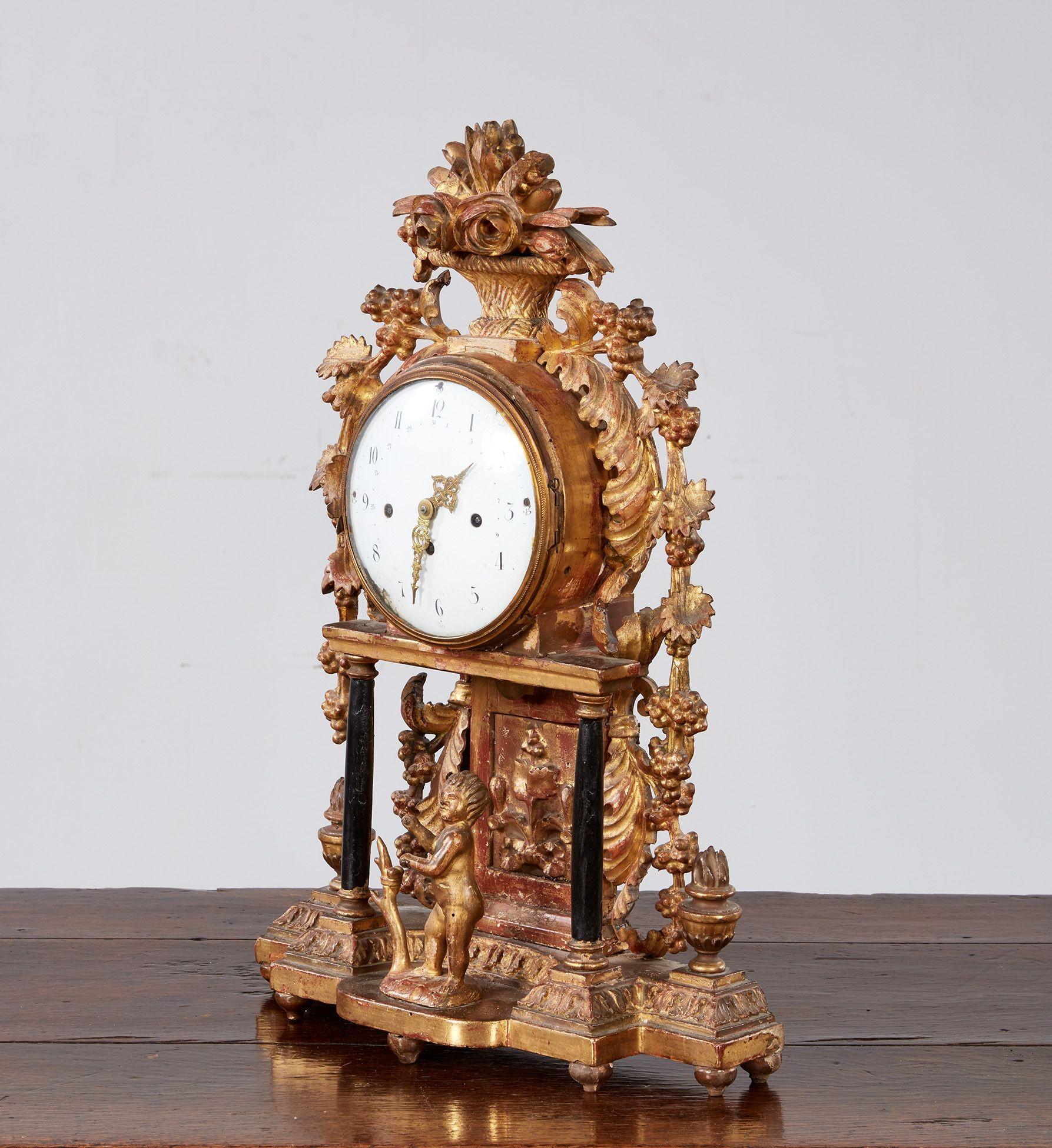 Fine giltwood mantel or shelf clock with carved floral basket crest, the enamel dial with gilt hour and minute hands, surmounted by carved grape vines and standing on platform base with carved putti and flaming urns, Austrian or more likely