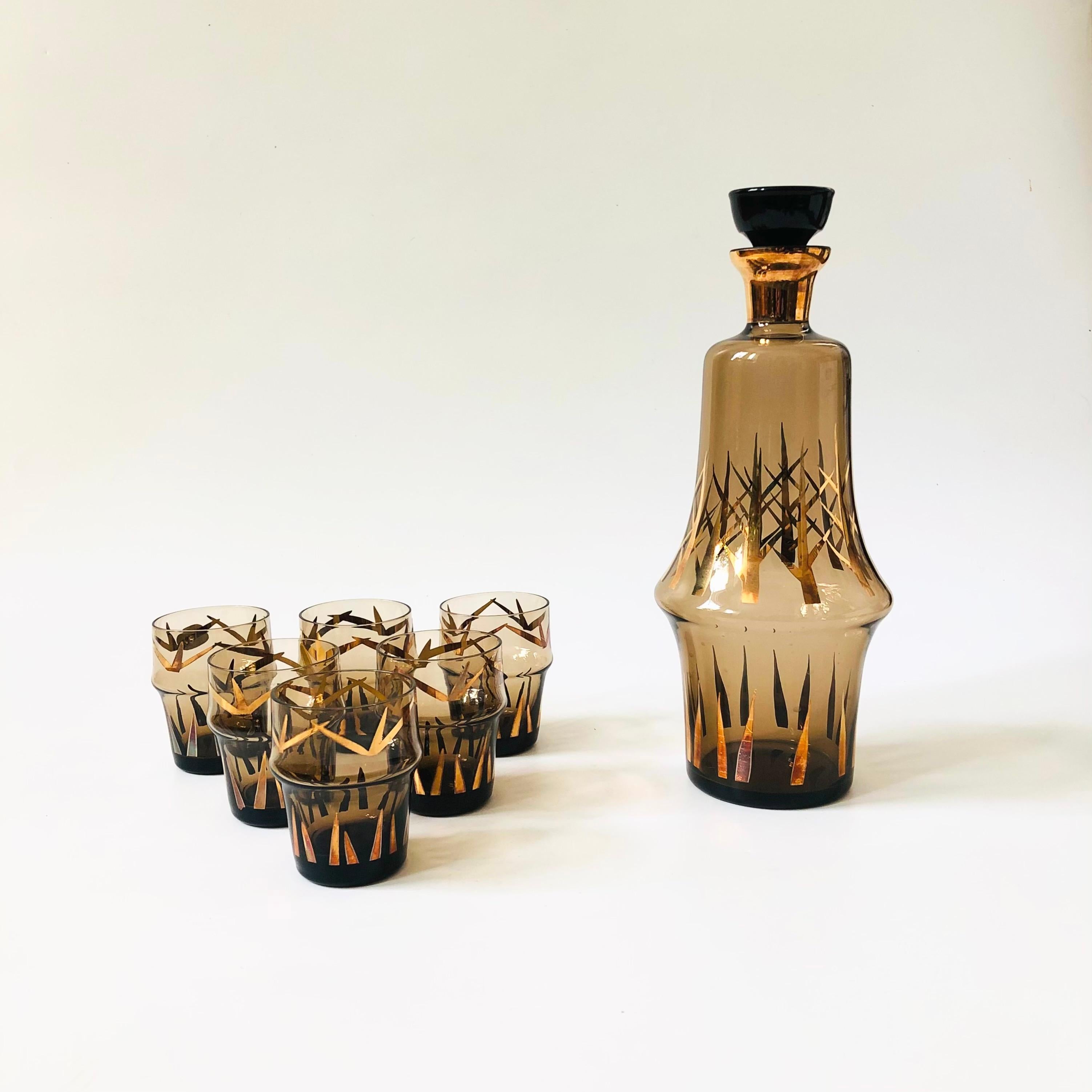 A vintage Bohemian crystal decanter set. Includes 1 large decanter with a stopper and 6 cordials. Each piece has a lovely smokey gray color to the glass and is decorated in metallic gold. A couple of the original stickers are still attached, made in