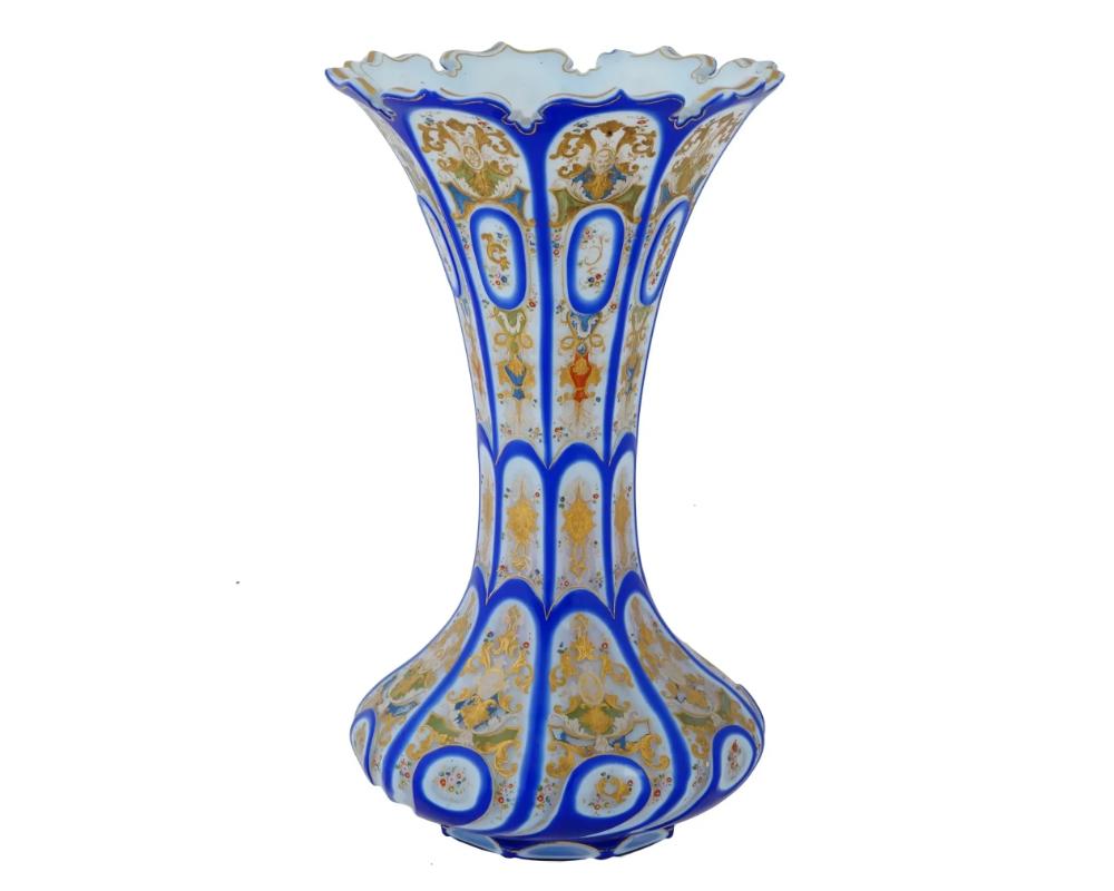 An antique Czech Bohemian blue overlay cut to clear opaline glass vase with a fluted mouth. The ware is adorned with hand enamel polychrome panels depicting medallions surrounded by floral, foliage, and scrollwork motifs, and decorated with gilded