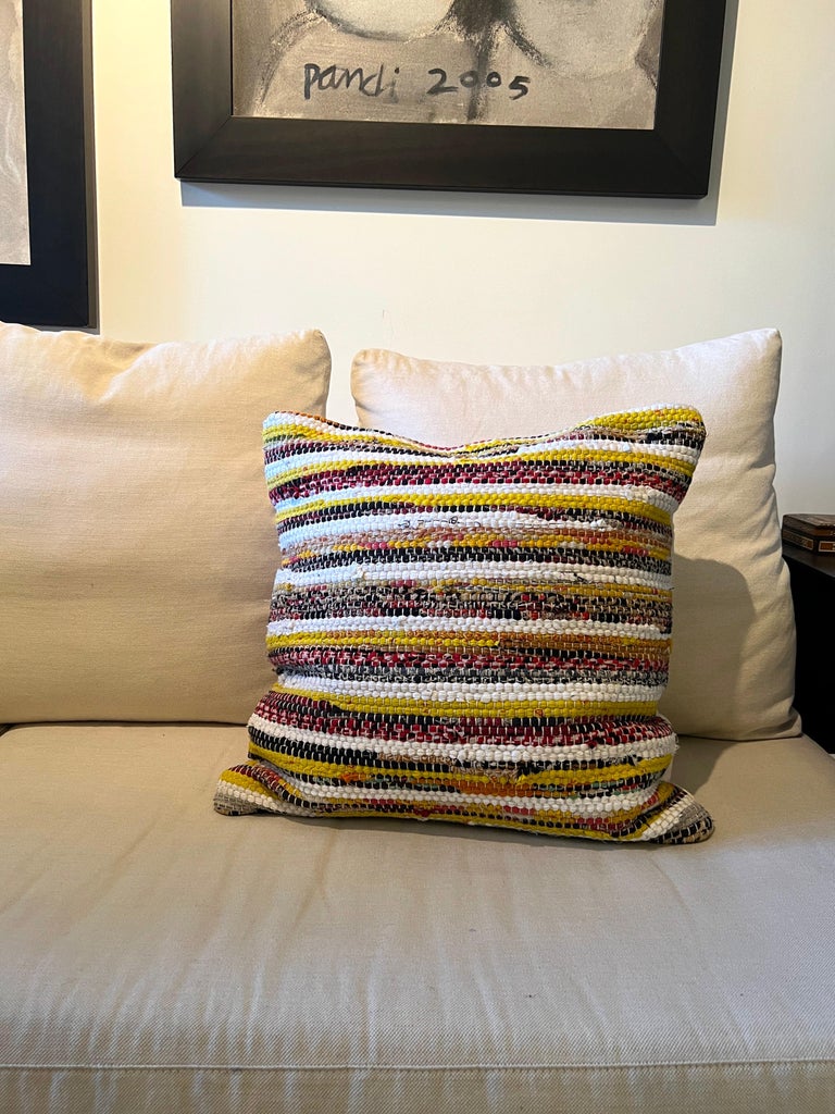 Bohemian textile decorative pillow comprised of handwoven vintage hemp with multicolor stripe design in twisted bouclé yarns. Features horizontal stripes in hues of red, yellow, white, black, and taupe. The reverse side is made of a neutral, cream
