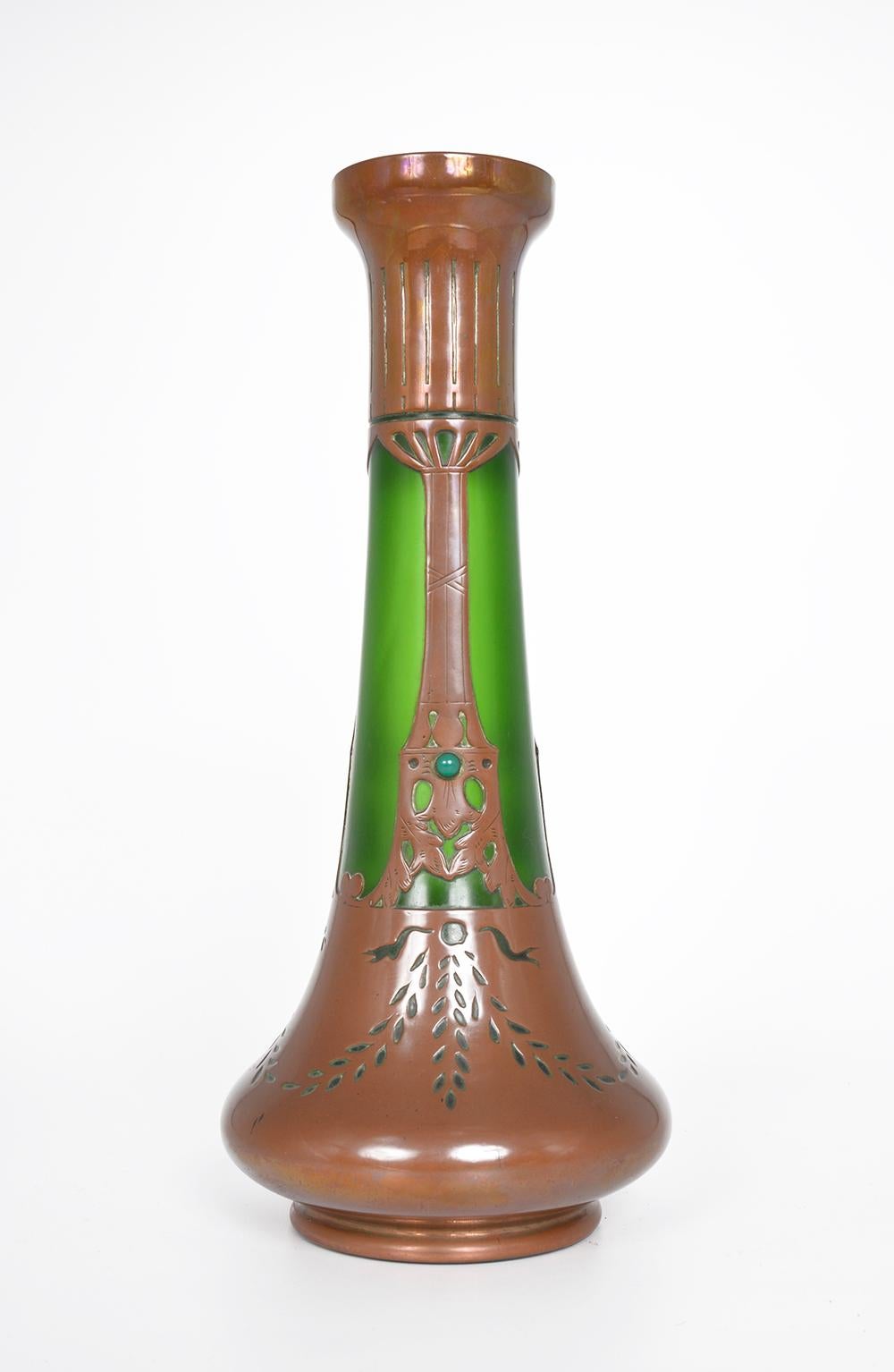 This is a large hand blown emerald green opaque glass vase with applied open work copper overlay decoration, which is likely to have been manufactured in Austria around the 1900s. Its stunning linear surface pattern reveals the artistic influence of