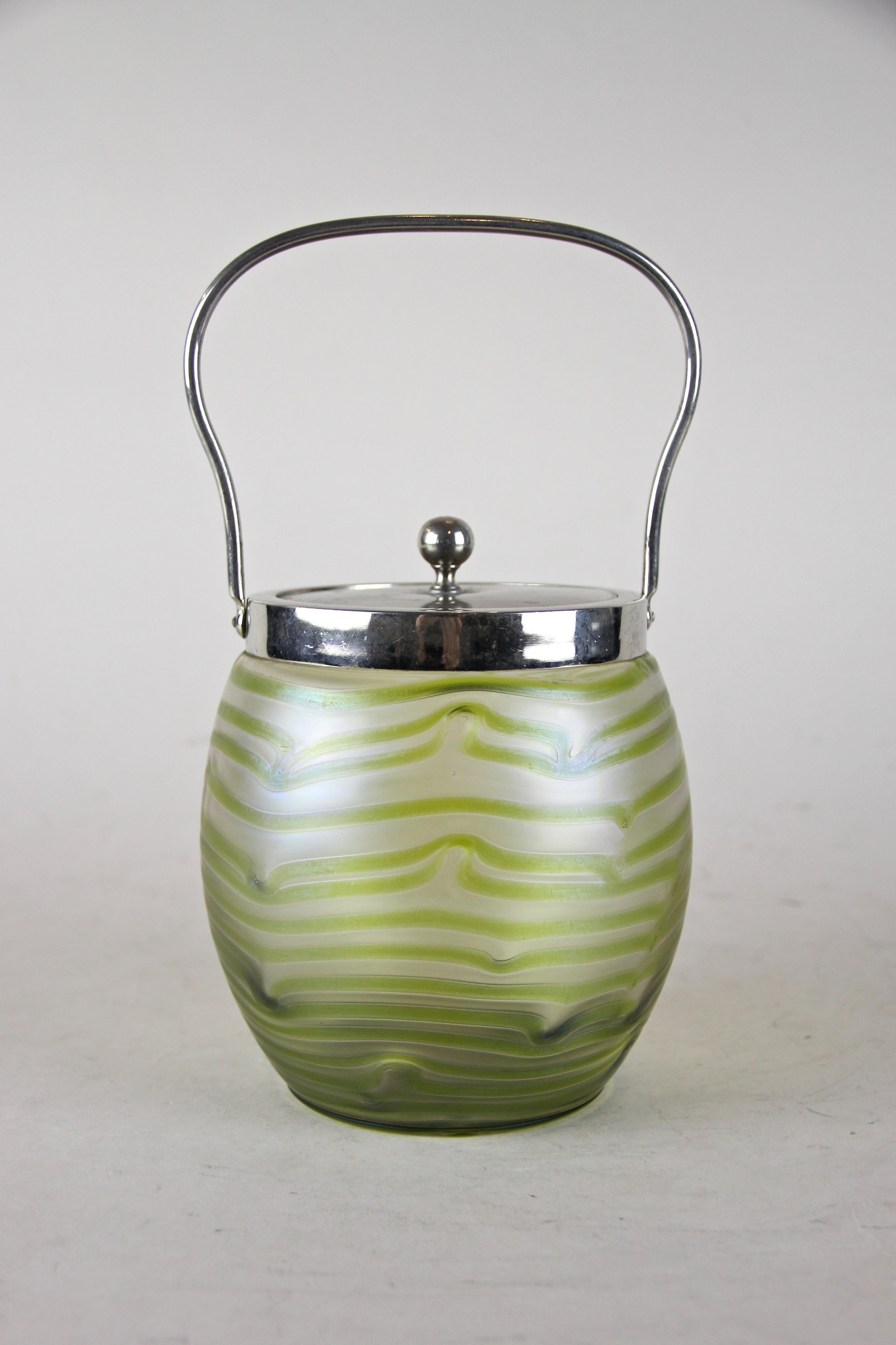 Decorative glass jar by Palme König with lid from the early 20th century out of Bohemia. The gorgeous iridescent glass body shimmers in different colors by showing beautiful green lines. A chromed mounting with slim handle fits perfect to the artful