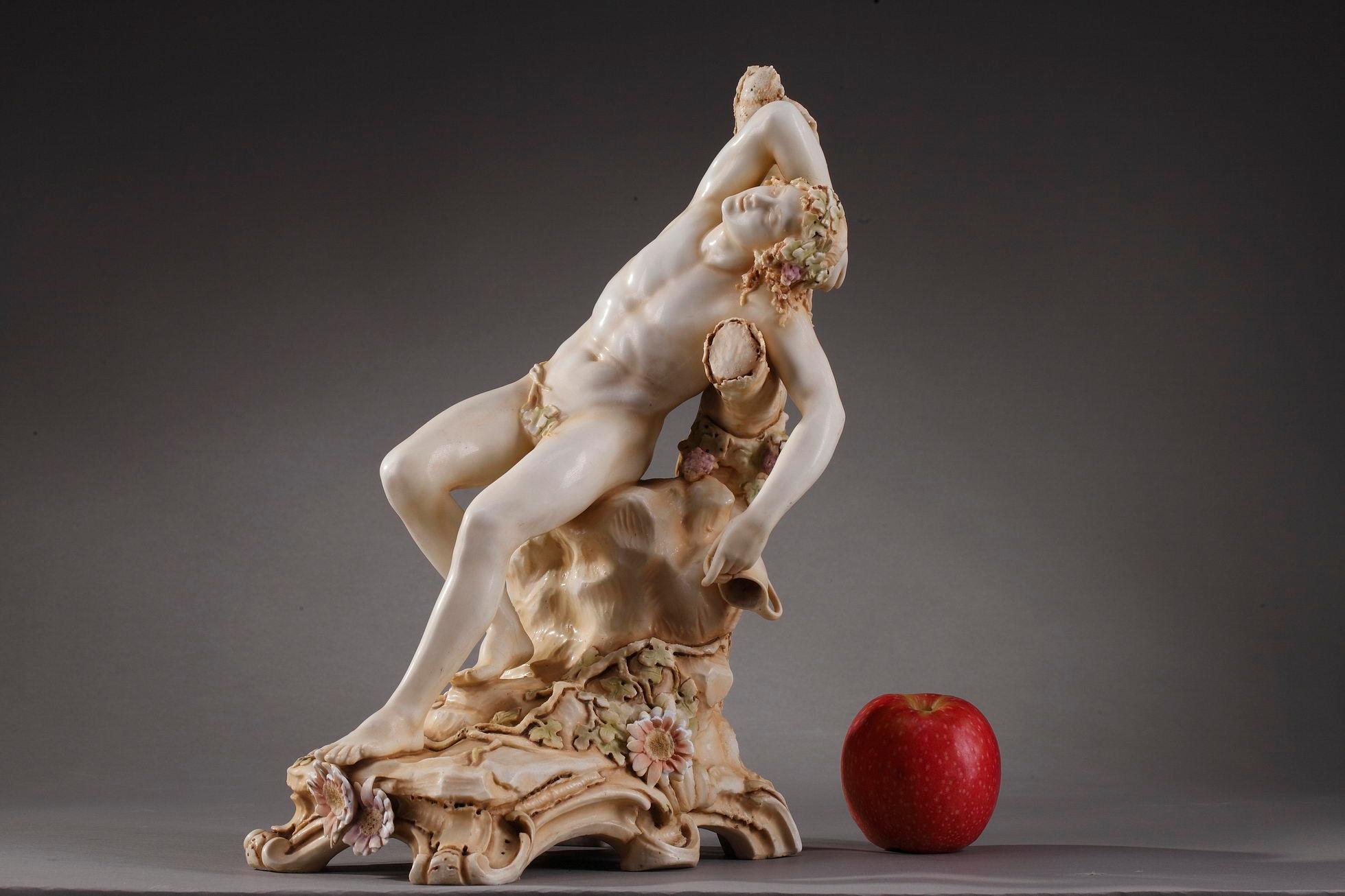 Small sculpture in Bohemian porcelain biscuit featuring Bacchus or Dionysus, the Ancient Greek god of wine and fertility, lying on a trunk decorated with cluster of grapes. He is naked, and wears a crown of vine leaves. The young god holds an empty