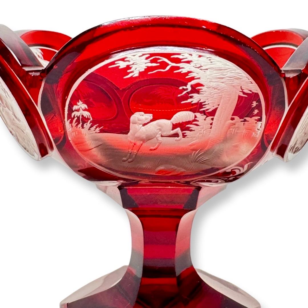 This exceptional ruby-stained crystal bowl is a masterpiece of 19th-century Bohemian glassmaking, attributed to the renowned master Karl Pfohl. The piece stands out for its exquisite engravings depicting hunting scenes and natural landscapes,