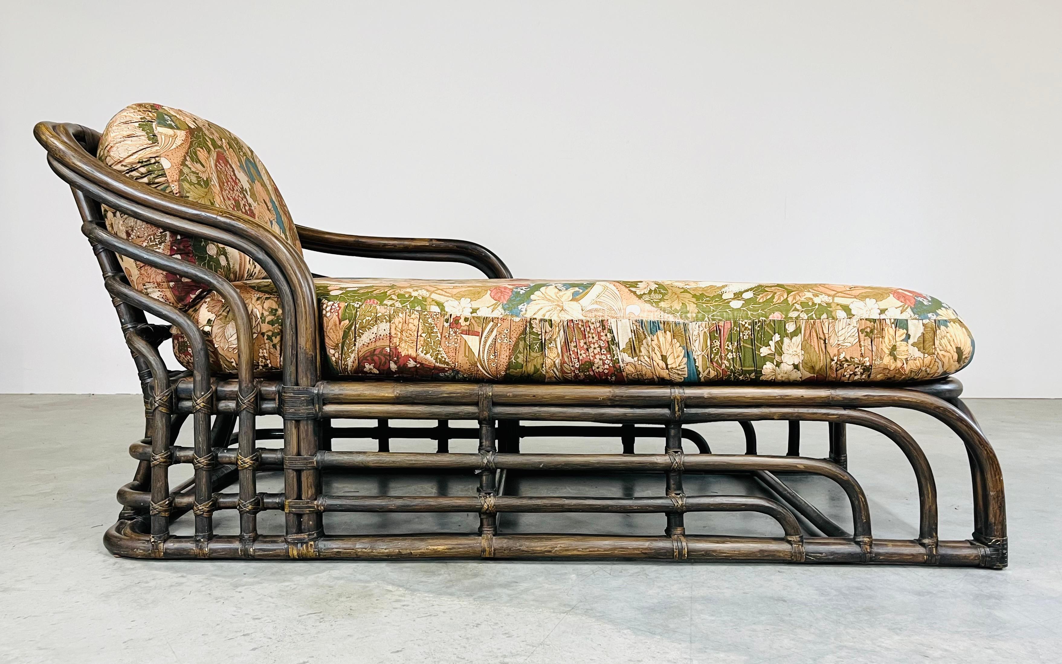 Mid-century chaise lounge having sculptural bamboo frame with leather joinery and stunning lines with beautiful chintz floral upholstery. The chaise features a shorter right armrest for easy entry and exit as well as a wooden platform cushion