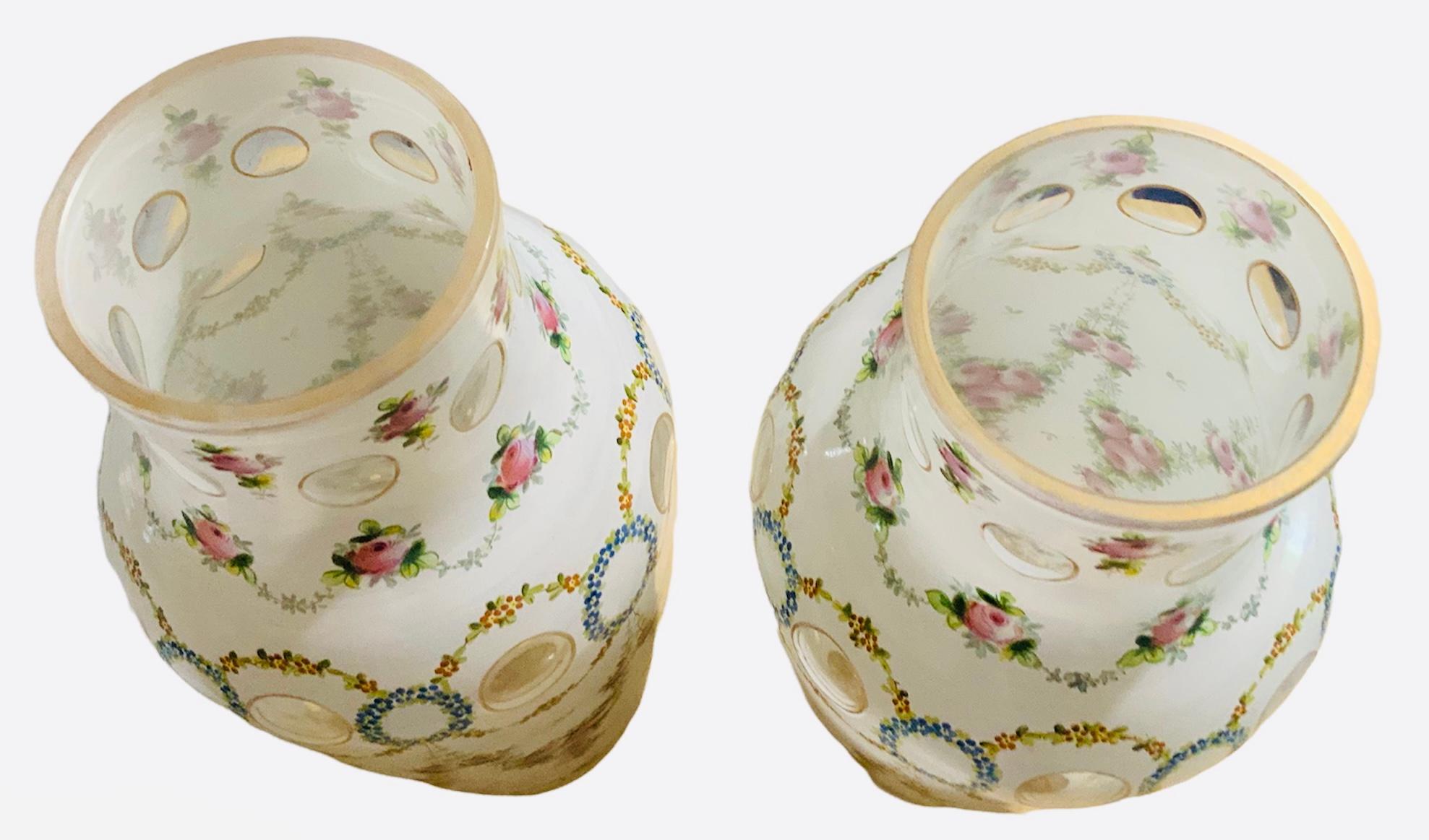 This is a little heavy pair of opaline overlay crystal vases. They have a cylindrical neck with urn shaped bodies. They are decorated with coin dots at the neck and in the upper body. But also oval dots highlighted the bottom. Also, some garlands of