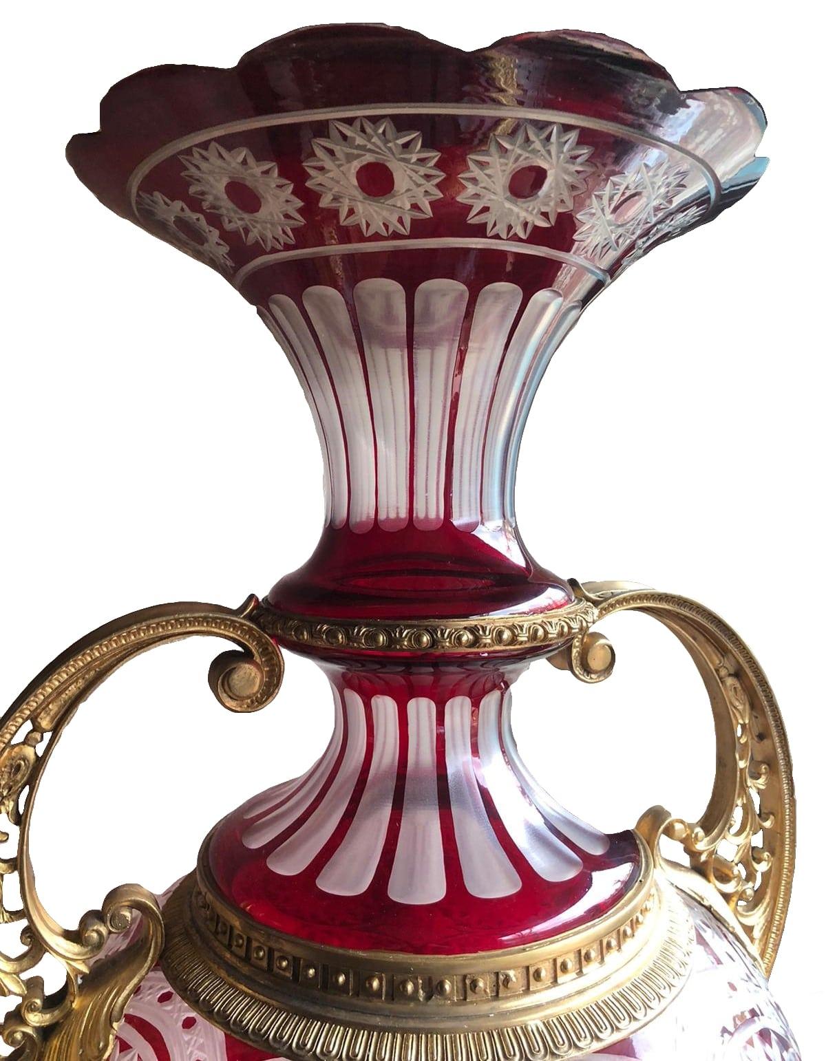 A pair of monumental Bohemain cut crystal ruby red vases in the manner of Moser. Gilt bronze and cut crystal vases perfect for gracing entrance halls or centre pieces. Solid cut crystal vases with ribboned tops accompanied with heavy gold gilding