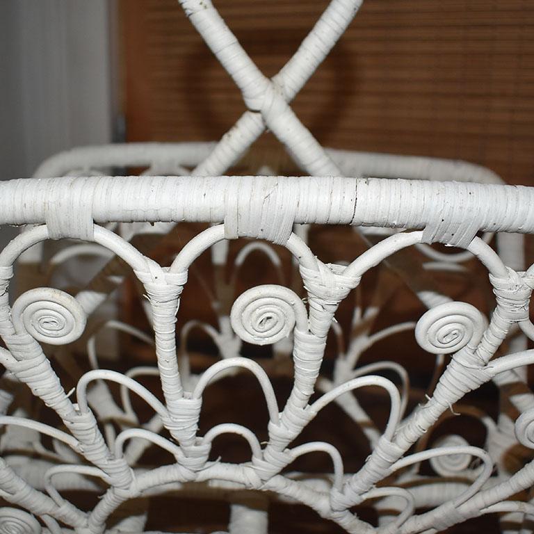 A whimsical white-wrapped rattan magazine rack. This piece reminds us of the 1970s and the popular peacock chairs that seem to define that era. This piece was painted white in its previous life and features swirls of wrapped rattan throughout.