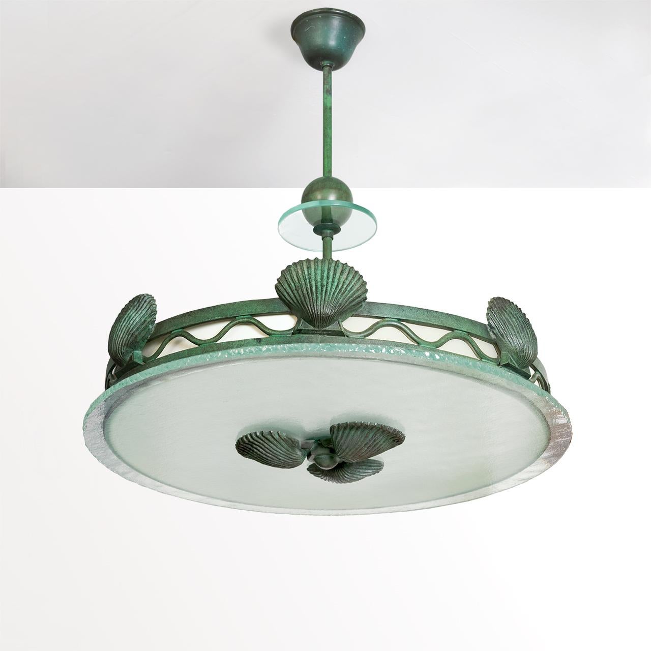Swedish Art Deco patinated metal pendant with shell motif. The fixtures frame is decorated with a series of shells which are separated by wave like lines which holds a paper shade behind it. The stem features a glass disk and a patinated floating