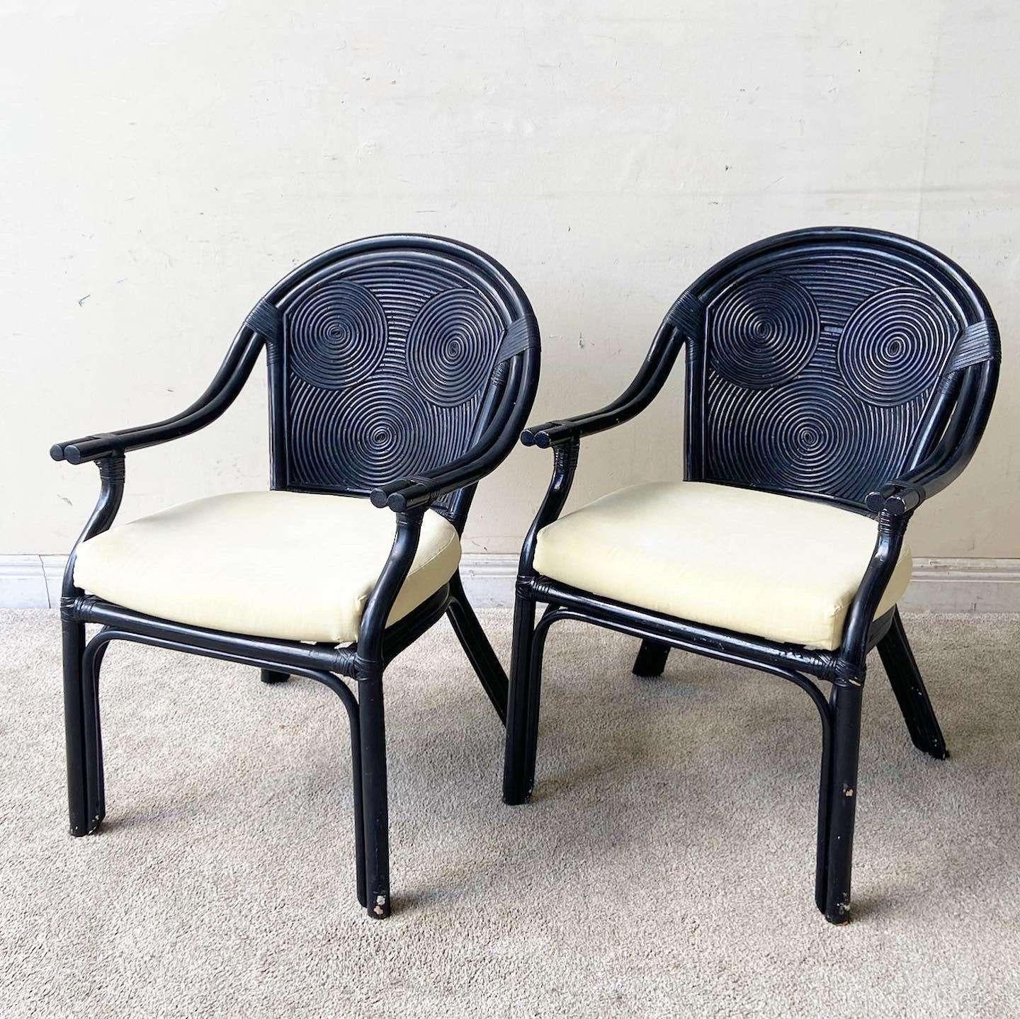 Exceptional vintage pair of bohemian pencil reed arm chairs. Each feature a black finish with a cream, off white seat cushion.
