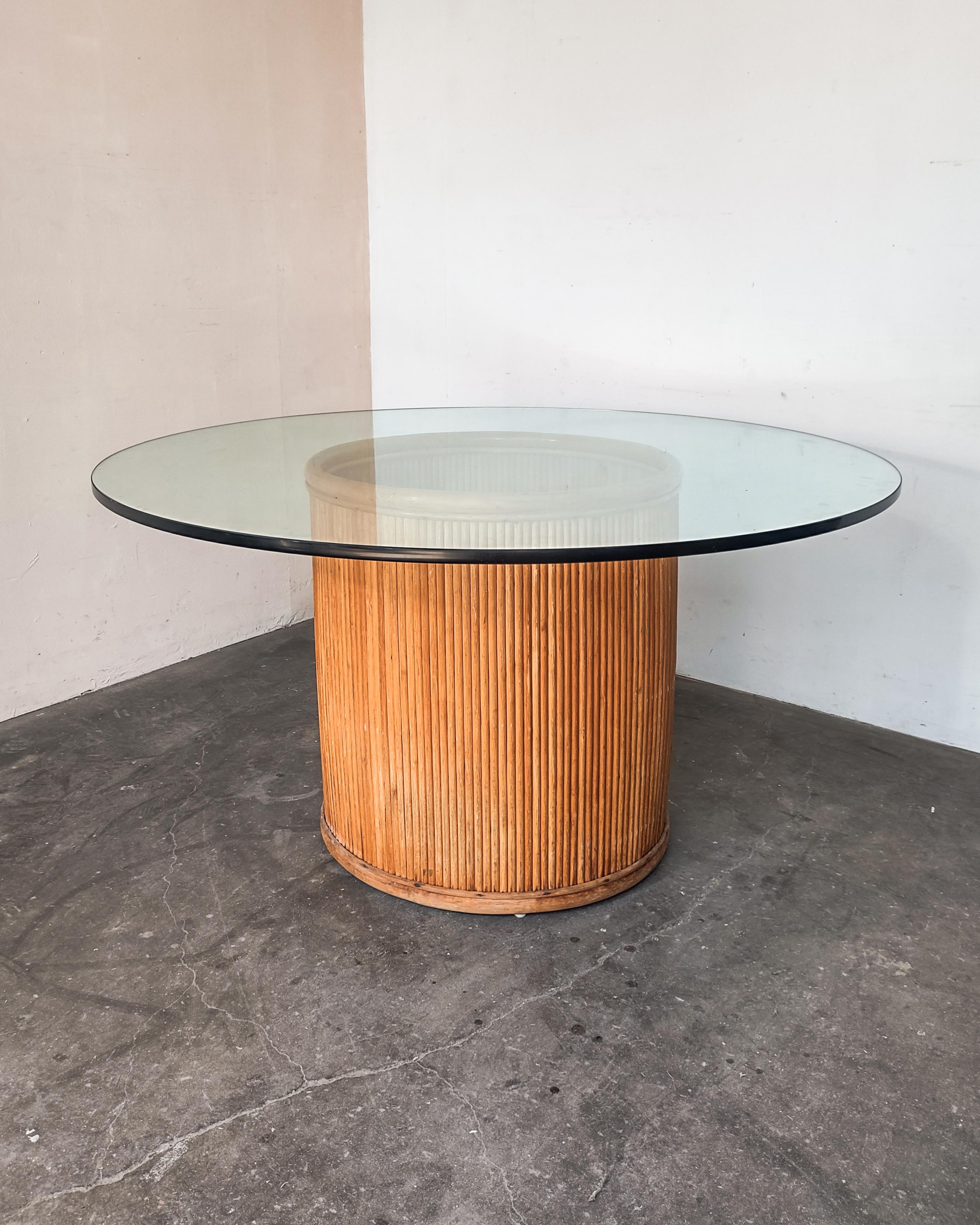 Split pencil reed dining table with glass top features a round split-reed rattan pedestal base and a thick glass table top. Overall great condition with some wear consistent with age.

Measures: 53-5/8