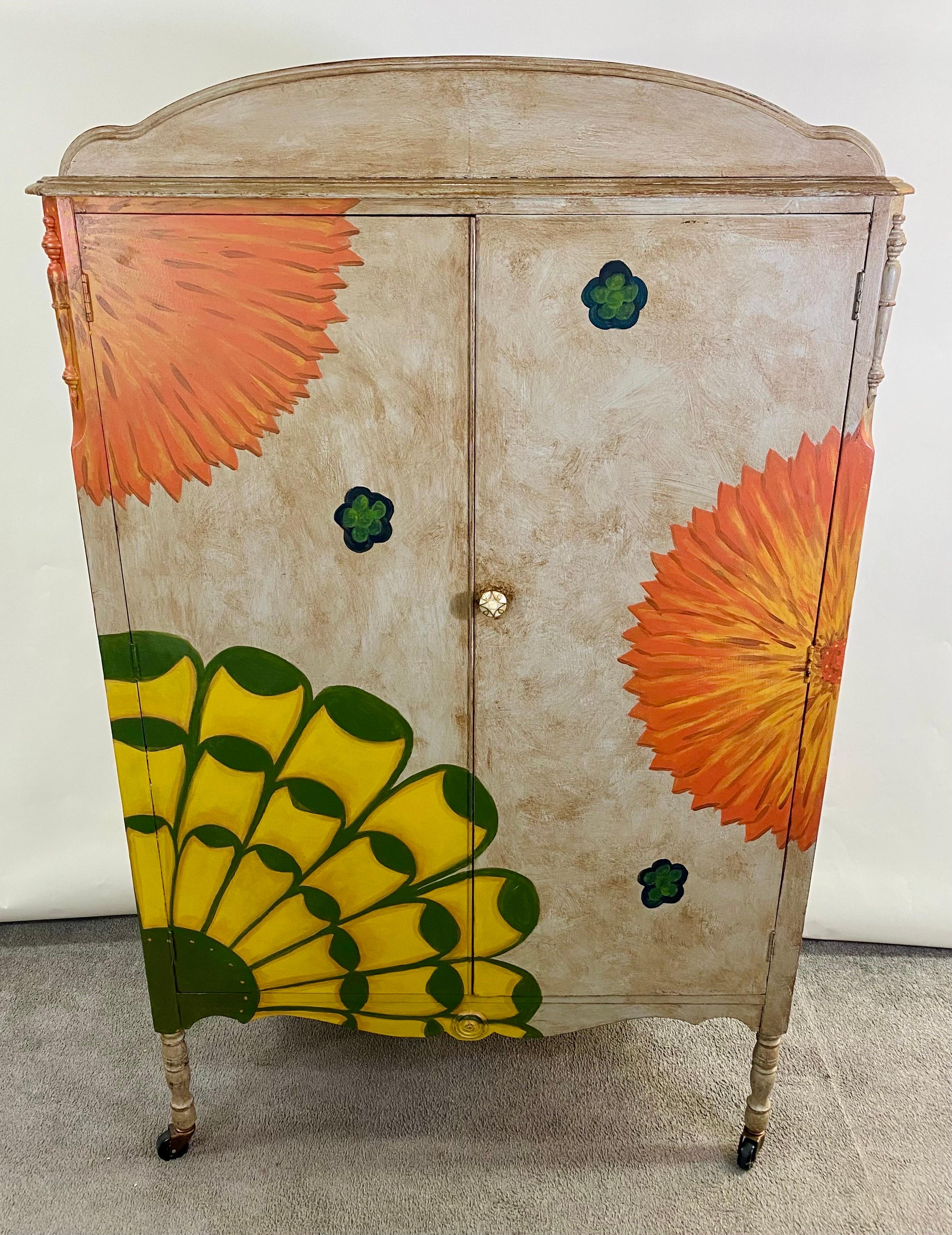 A whimsical boho chic armoire or wardrobe hand-painted in beige with orange , green and yellow flowers motifs on beige background. The armoire is standing on 4 wheeled legs allowing mobility to move and use easily in your space. The inside of the