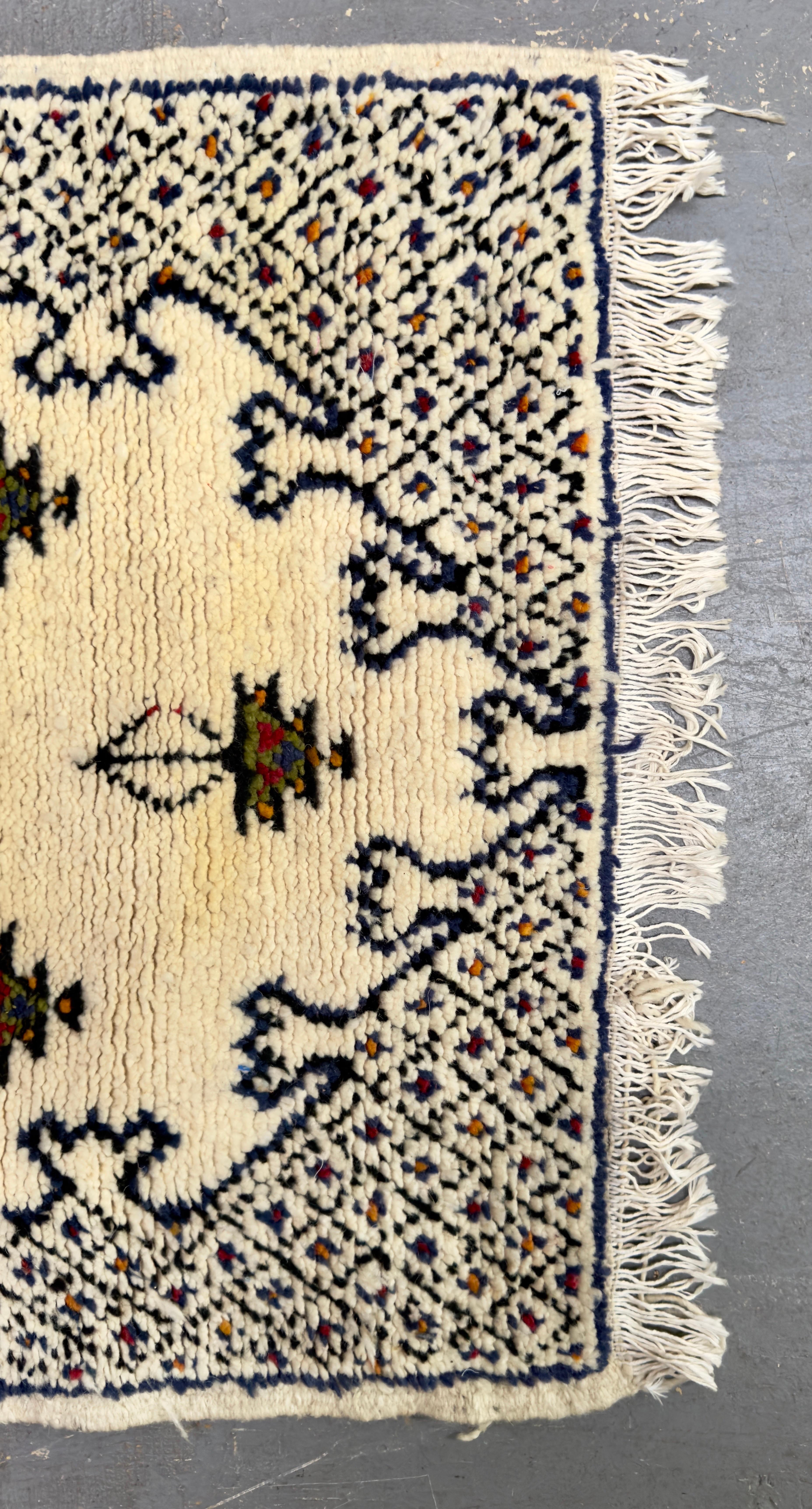 Un joli petit tapis marocain tribal Boho Chic vintage présentant des motifs géométriques et tribaux en noir avec un soupçon de rouge et de vert sur un fond blanc. Le tapis est tissé à la main en utilisant de la laine de mouton de la plus haute