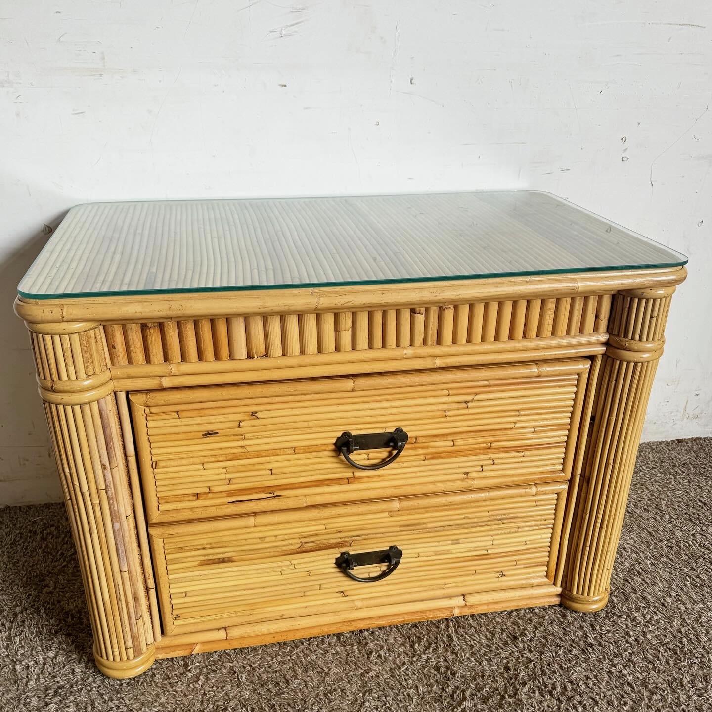 Introduce a touch of natural elegance to your bedroom with this Boho Chic Rattan Nightstand/Commode. Featuring intricate pencil reed detailing and a sleek glass top, this vintage piece blends functionality with bohemian style. The two spacious