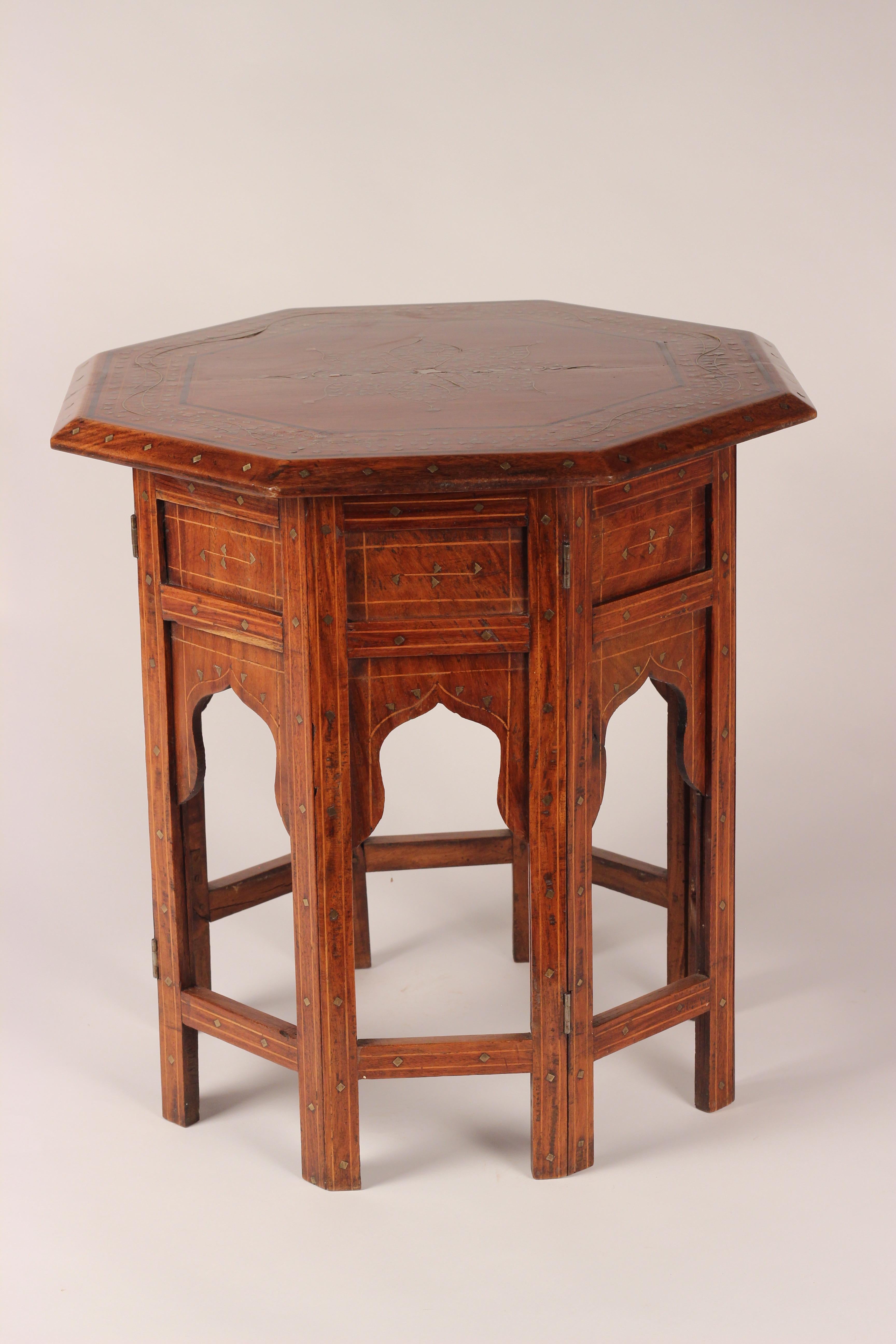 An octagonal side or drinks table with string inlay and brass inlay filigree top. Similarly decorated to folding base, which reduces the volume further, for ease of shipping. A striking warm and crafted piece of Anglo Indian, circa 1900. This table