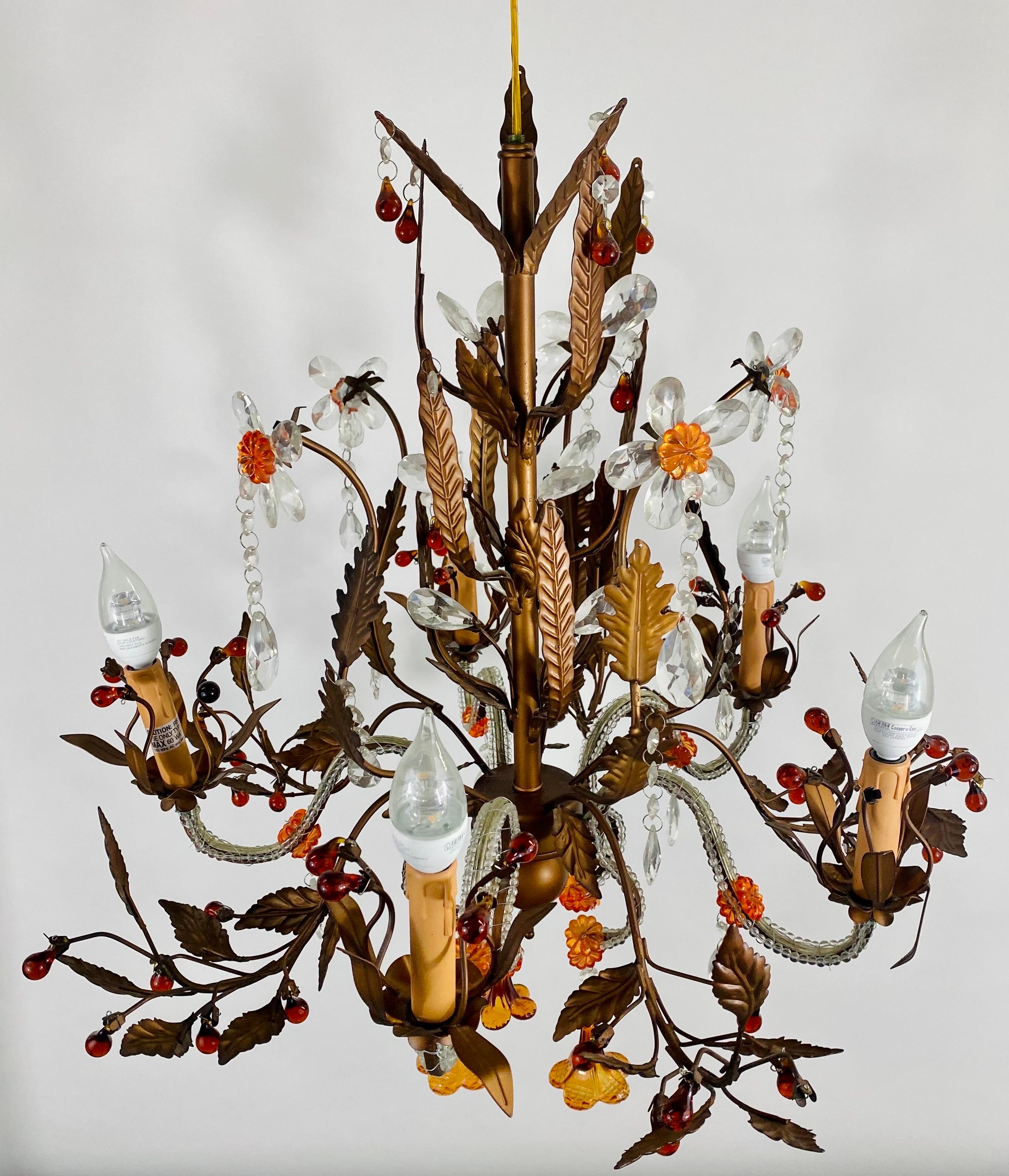 An exquisite Boho chic 1970's tole metal chandelier. The chandelier features faux crystal white lilies land orange flowers embellishing the leaves design of the chandelier painted in brown. The arms are elegantly covered in beads adding style to