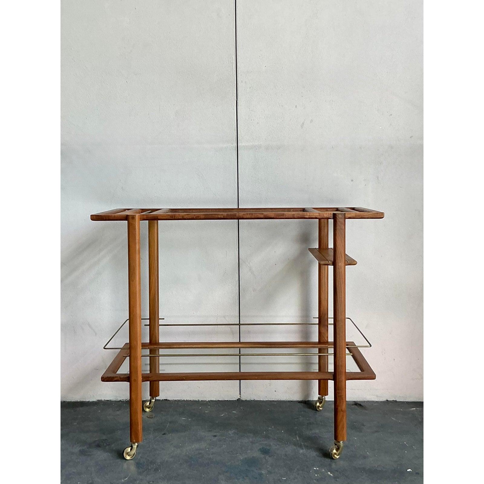 Serve up style and sophistication with this stunning vintage teak bar cart. A beautiful example of Mid-Century design, this piece is masterfully crafted from polished teak, showcasing a rich, warm grain and clean, architectural lines that are a