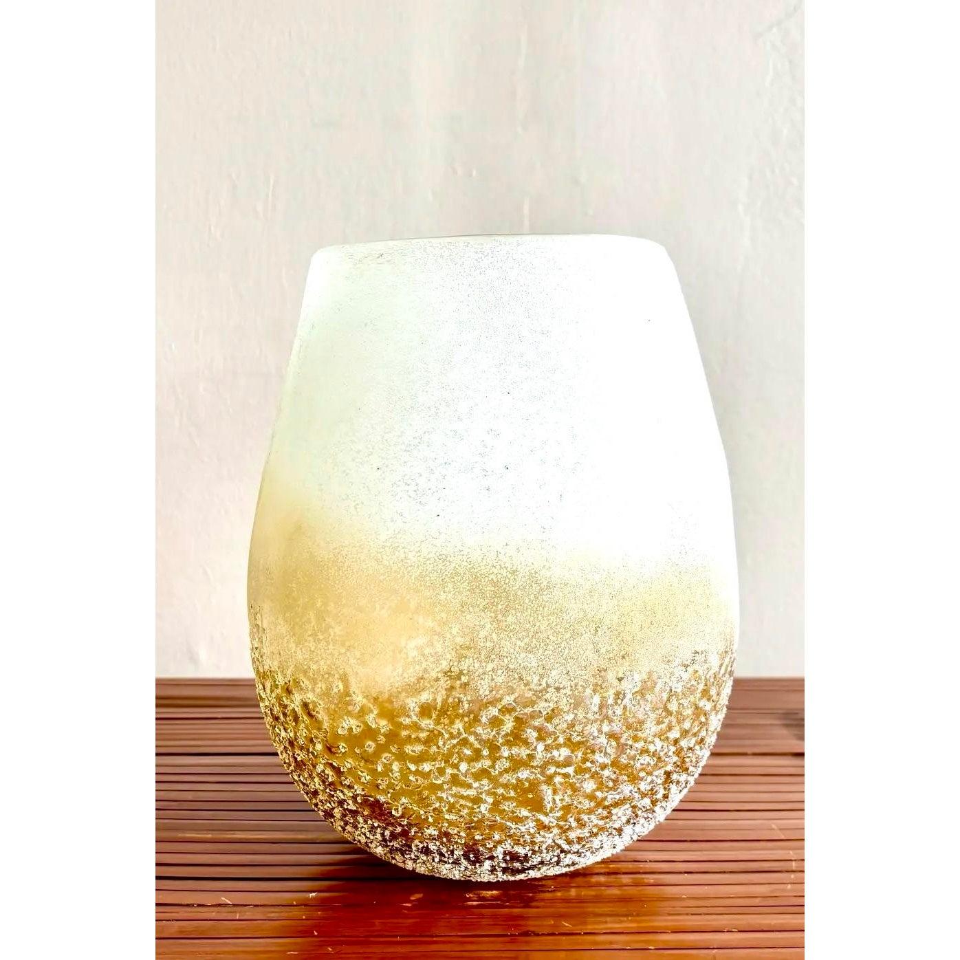 Un vaso in vetro soffiato a mano, lunatico e tattile, con un morbido ombré smerigliato che sfuma dal bianco latte all'ambra dorata. La metà inferiore presenta una superficie ruvida e testurizzata che ricorda il sale cristallizzato o la sabbia