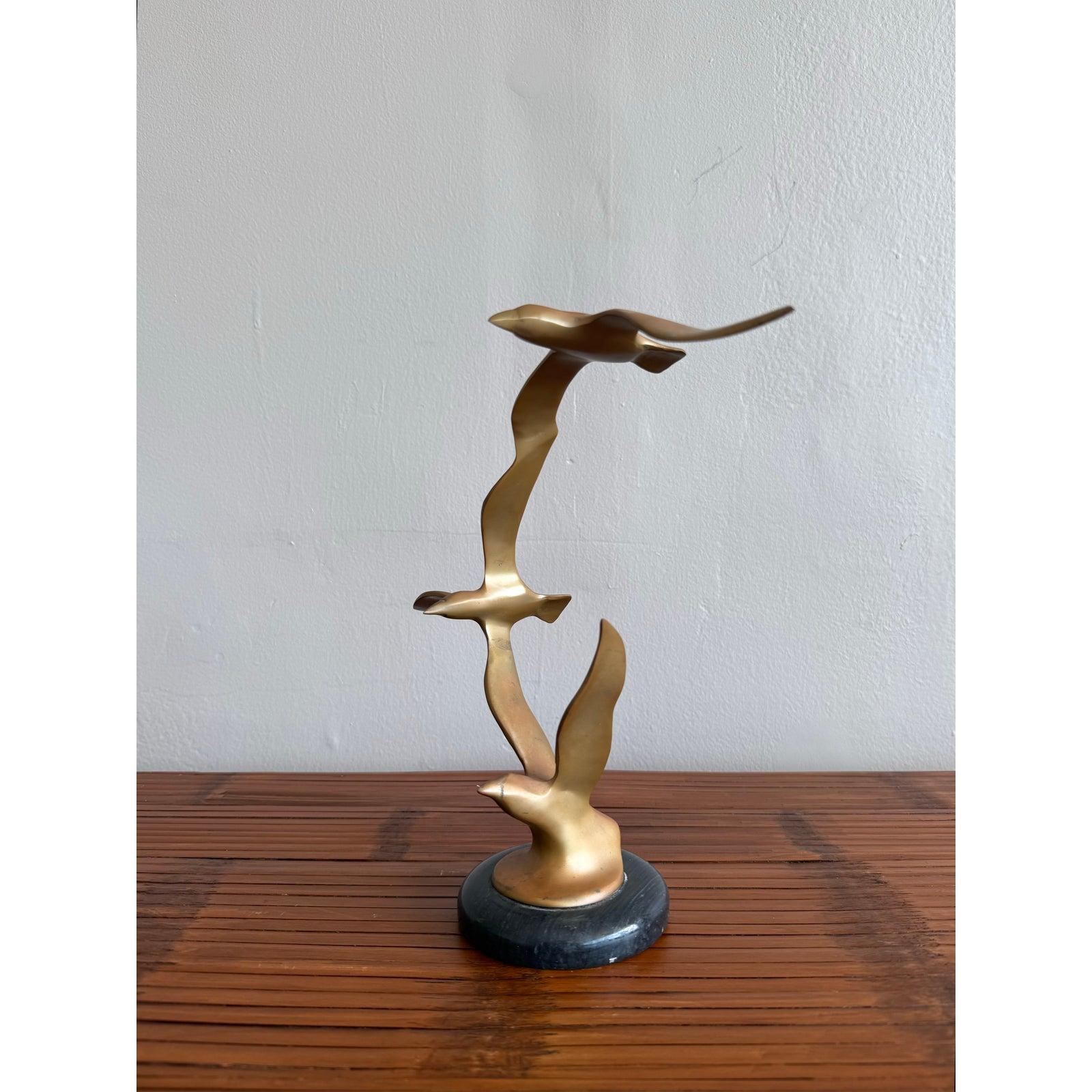Cette élégante sculpture en laiton capture l'essence de la liberté et du mouvement avec trois oiseaux minimalistes en vol, leurs ailes décrivant un arc gracieux au-dessus d'une base arrondie en marbre noir. Inspiré par les formes modernes du milieu