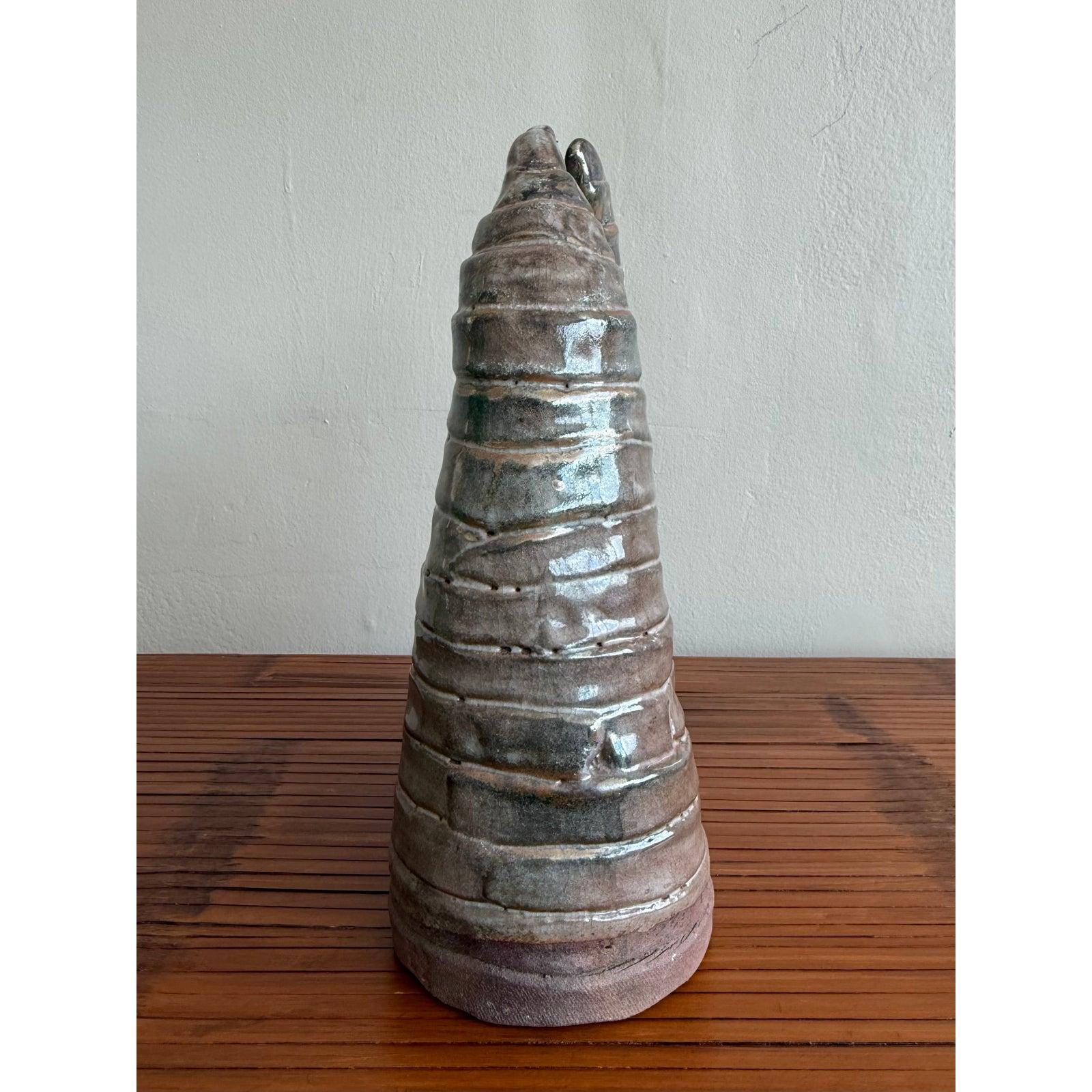 Diese einzigartige Boho-Keramikskulptur bringt eine erdige, strukturierte Präsenz in jeden Raum. Mit ihrer symmetrischen, organischen Form und dem zentralen Schlitz wirkt die Arbeit sowohl antik als auch futuristisch und erinnert an natürliche