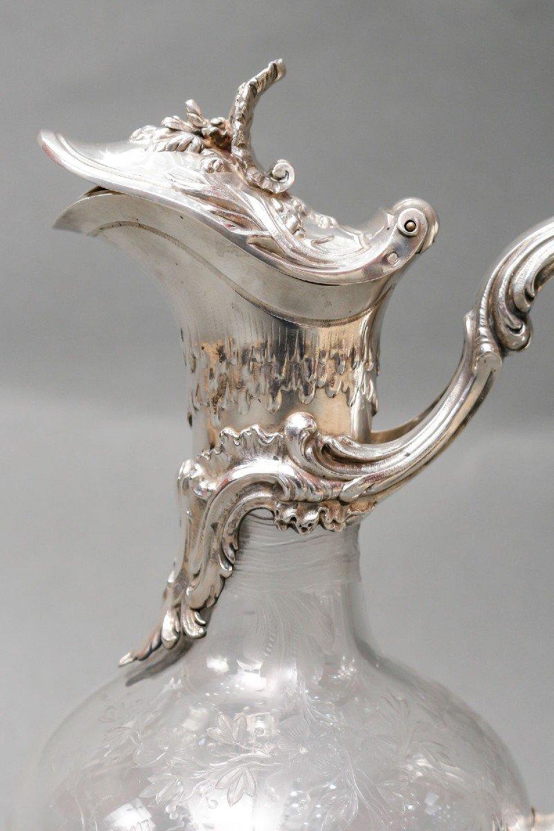 Crystal and silver ewer. The crystal is encased in a solid silver setting, the base rests on four scrolled feet and is chiseled with a rich decoration of waves and foliage, as well as the handle and the neck. The crystal is engraved with an acid