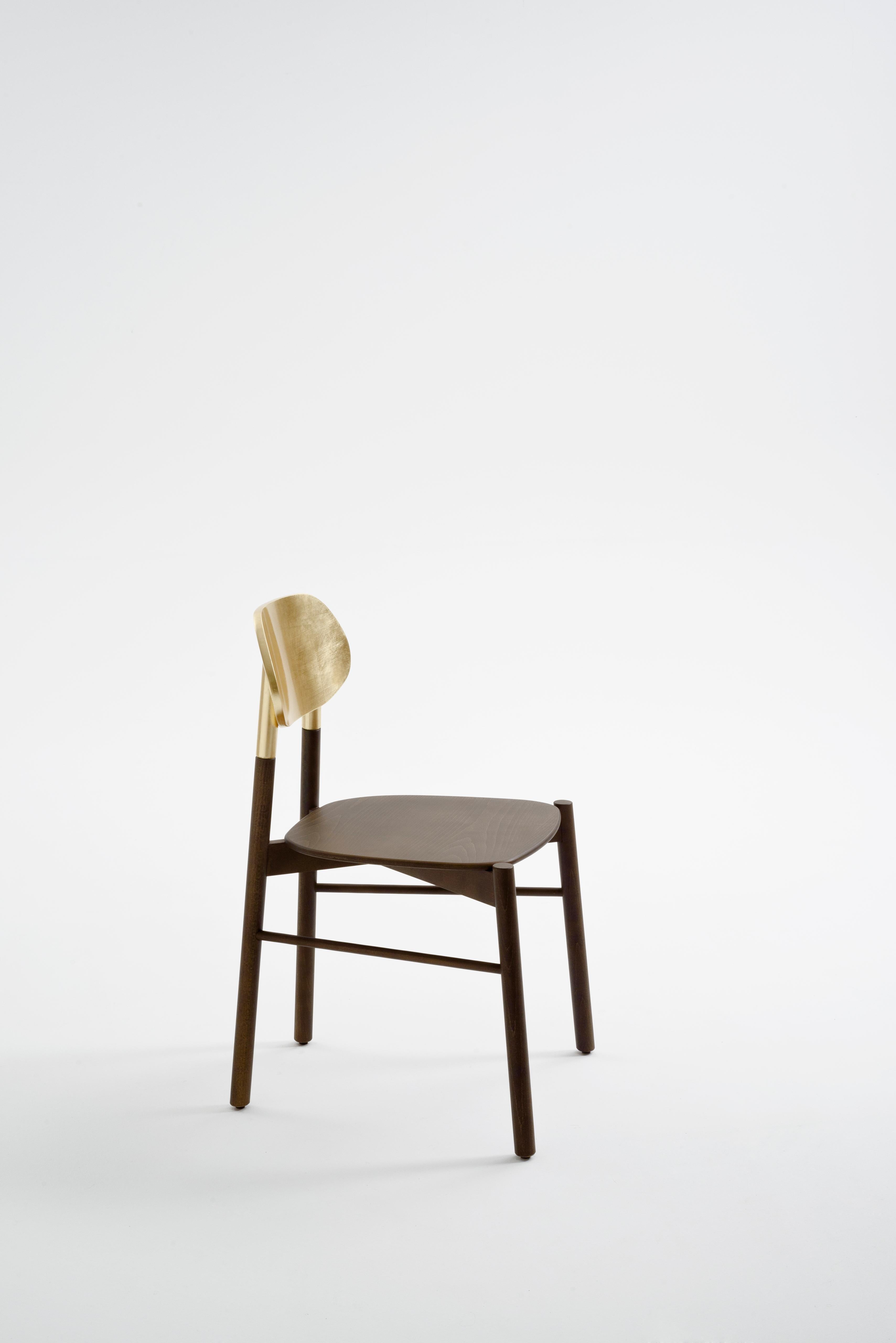 Dies ist ein Satz von 2 Stühlen, verpackt in einer einzigen Schachtel. Ein essentieller Stuhl in der Form A, der durch die Struktur aus Nussbaumholz und die authentische, handgefertigte Rückenlehne aus Blattgold wertvoll ist. Er ist äußerst bequem