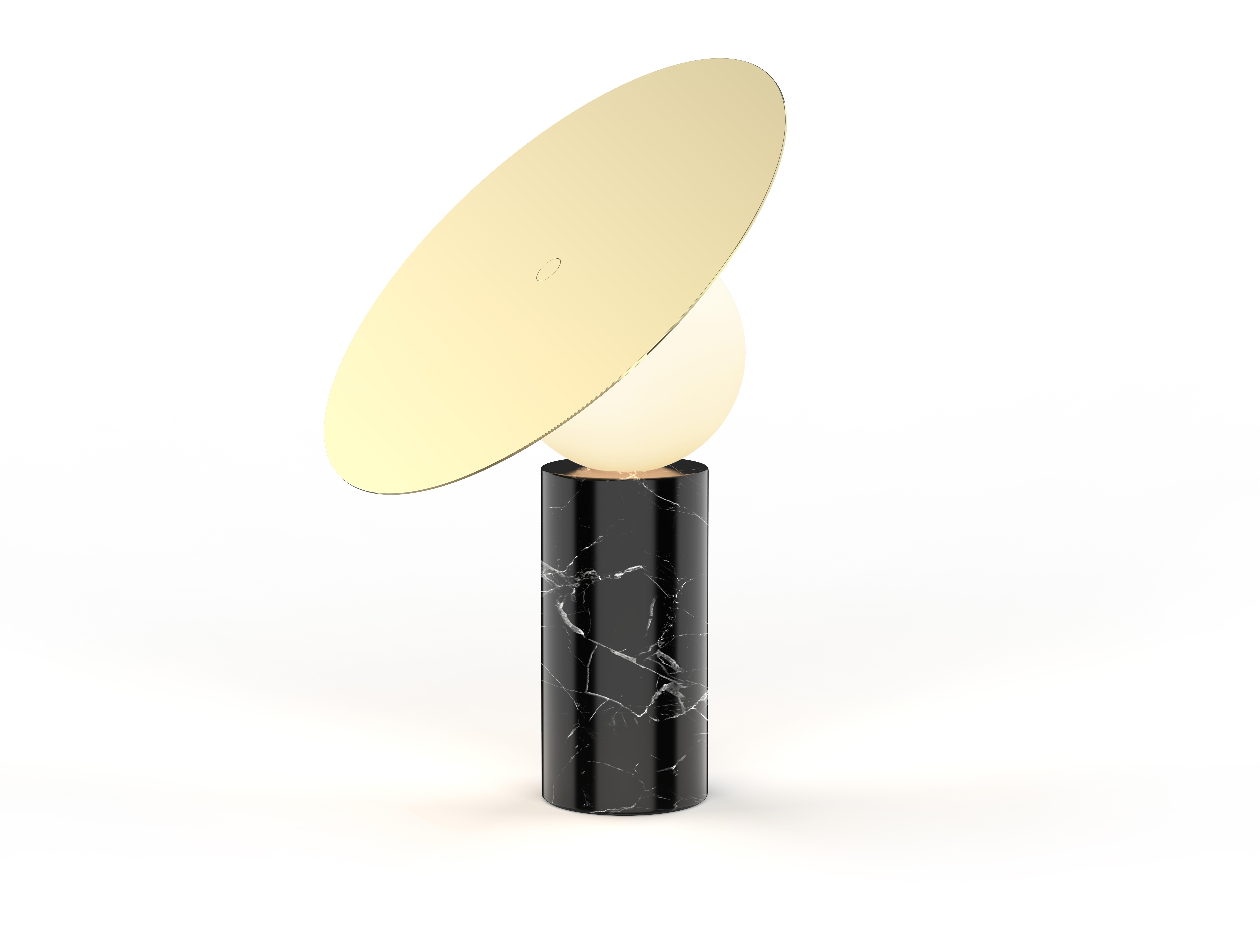 La silhouette iconique de la table disque Bola est définie par son élégant abat-jour en acier inoxydable chromé positionné à 45 degrés et surélevé par un diffuseur à globe en verre opalin qui semble flotter au-dessus de sa base cylindrique en