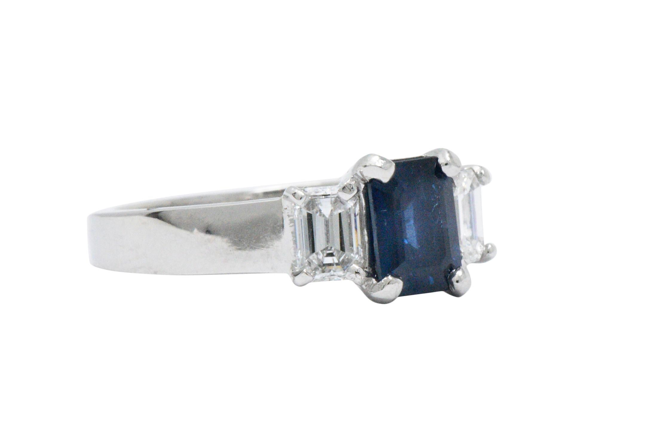 Centering an emerald cut sapphire weighing approximately 1.10 carats, deep soft rich royal blue

Flanked by 2 emerald cut diamonds weighing approximately 0.60 carats total, G color, VS to SI clarity

Clean geometric lines with a thick high polished