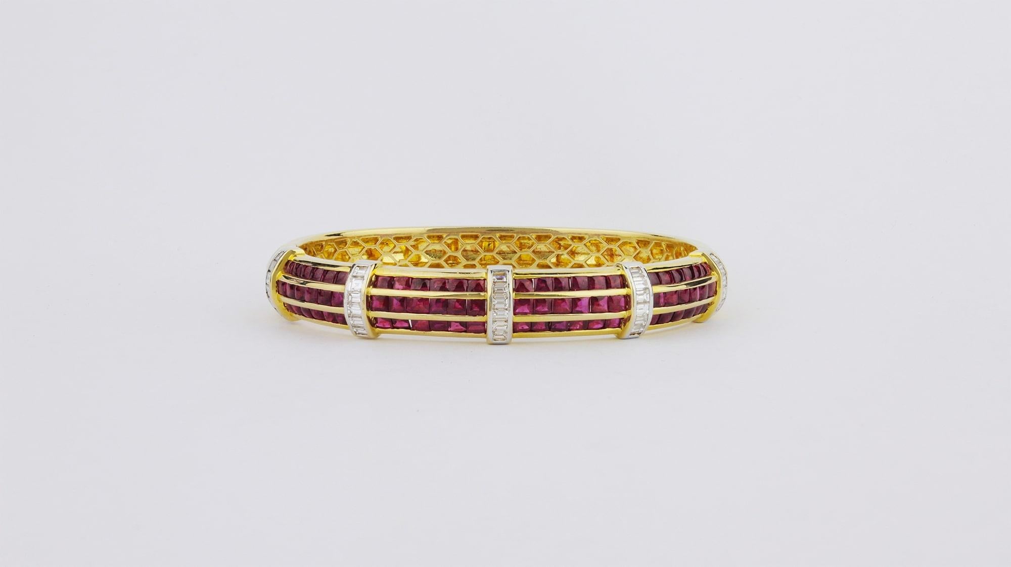 An exceptional ruby and diamond hinged bangle in 18kt yellow gold. Comprising of four panels of three rows of channel set square cabochon cut Burmese rubies interrupted by bands of platinum set baguette cut diamonds. The piece clasps with a tongue