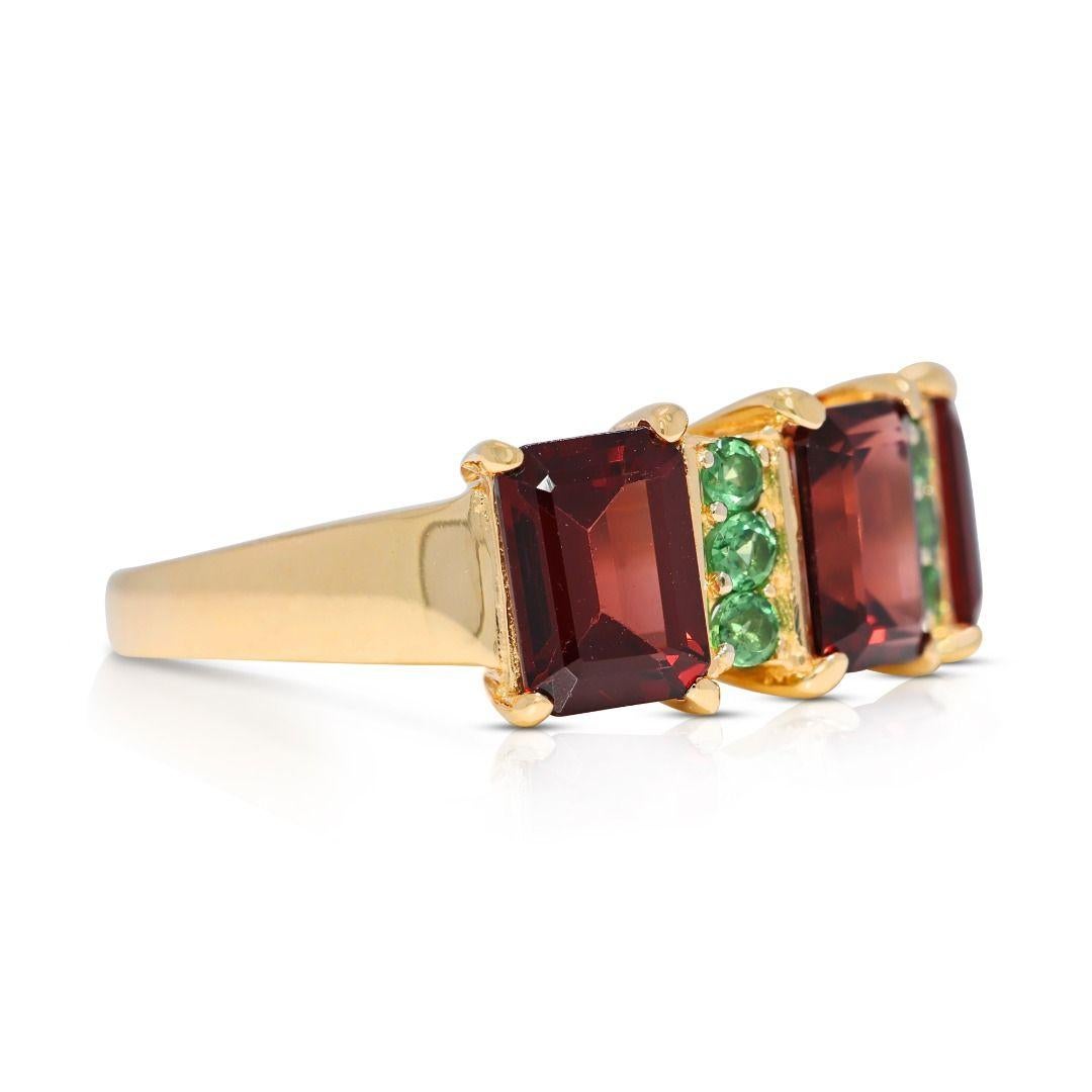 This stunning 14K yellow gold ring is a masterpiece of contrast and sophistication, featuring three emerald-cut red garnets, totaling 2.4 carats, radiating fiery brilliance at its core. Accentuating this bold centerpiece are six round brilliant-cut
