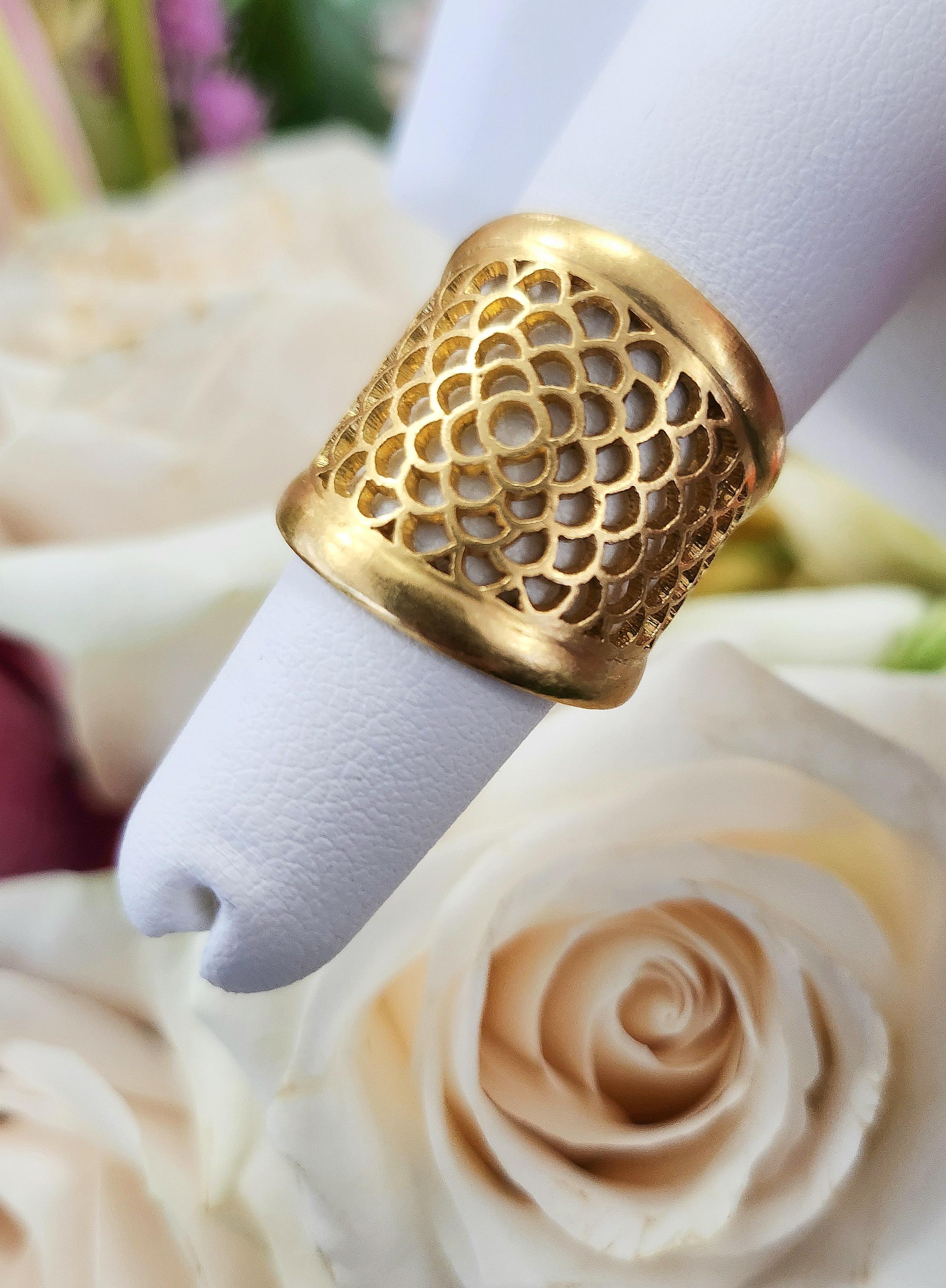 ieser außergewöhnliche Ring mit breitem Band verbindet auf luxuriöse Weise kühnes Design mit femininer Eleganz. Das aus massivem 22-karätigem Gelbgold gefertigte Schmuckstück weist ein wunderschön ausgeschnittenes Blumenmotiv auf, das der ansonsten