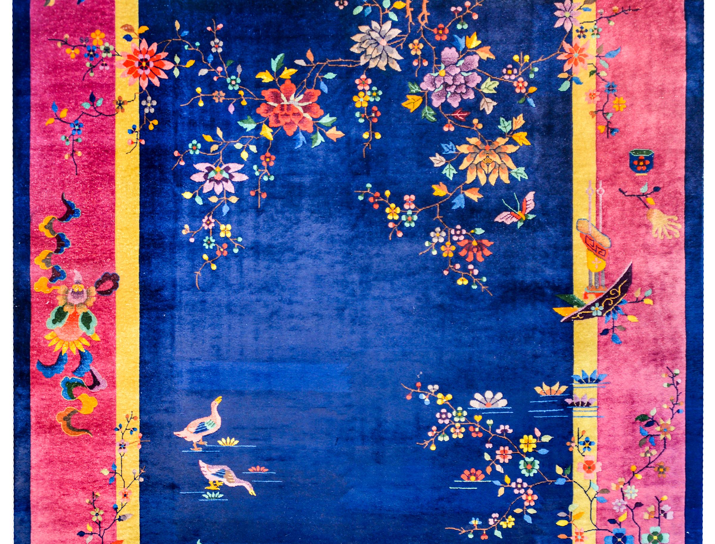 Un audacieux tapis Art Déco chinois du début du 20ème siècle avec un magnifique champ central indigo entouré d'une fine bande intérieure dorée, d'une large bande fuchsia et d'une fine bande extérieure indigo. Deux canards jouent dans l'eau du champ